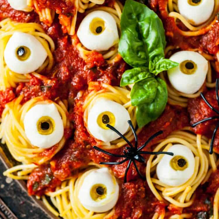 Halloween spaghetti with eyeballs, garnished with basil and plastic spiders.