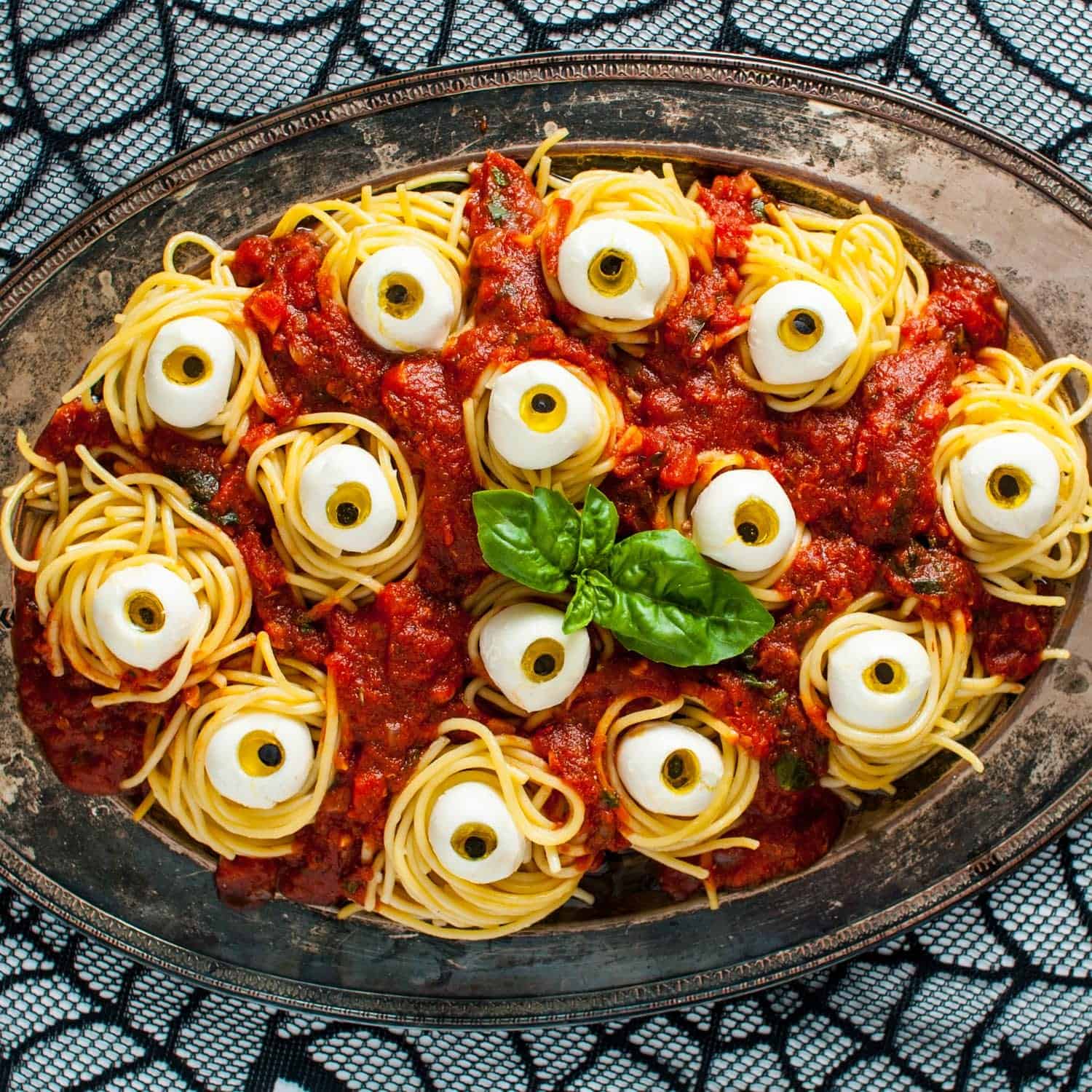 Halloween spaghetti on a rustic metal platter of spaghetti nests in tomato sauce. Inside each bundle of pasta is an edible eyeball made from mozzarella cheese.