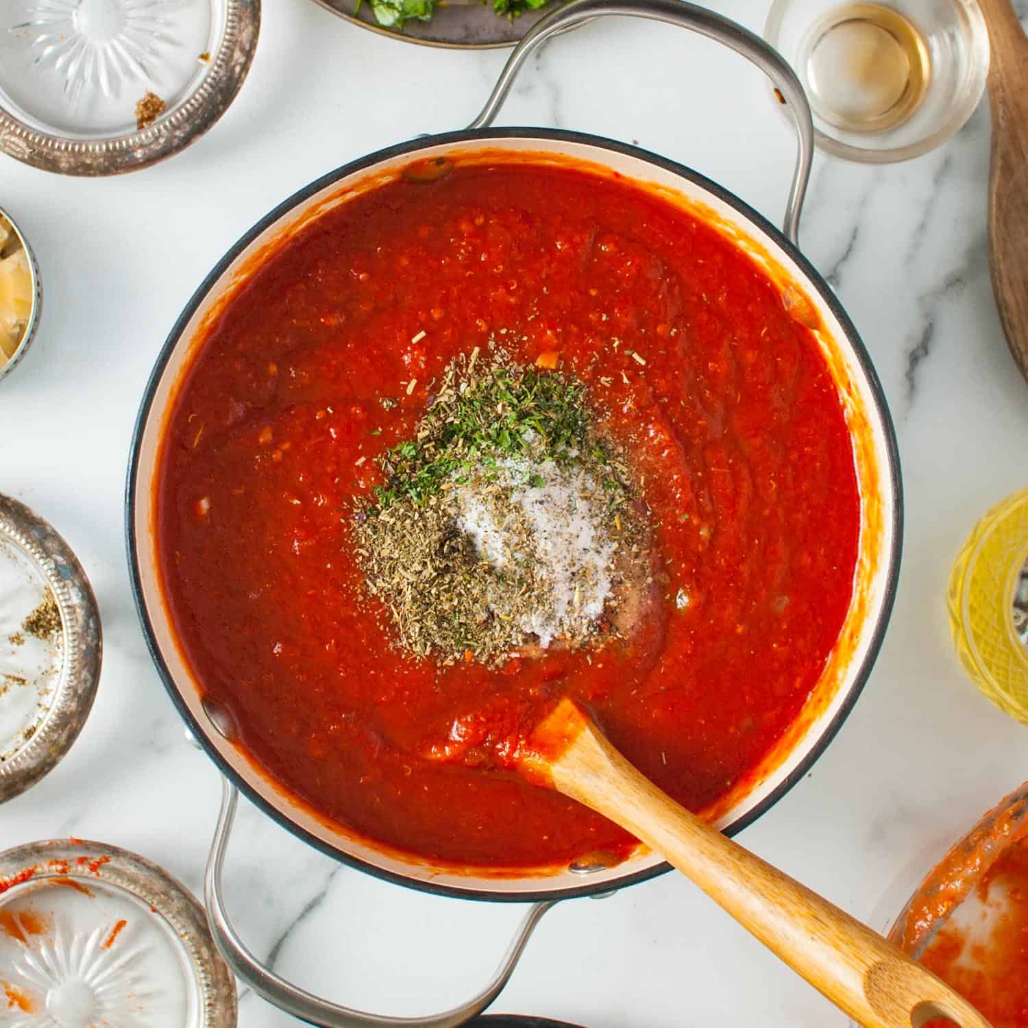 tomato sauce in a dutch oven, stirred with a wooden spoon. Seasonings and herbs have been added.