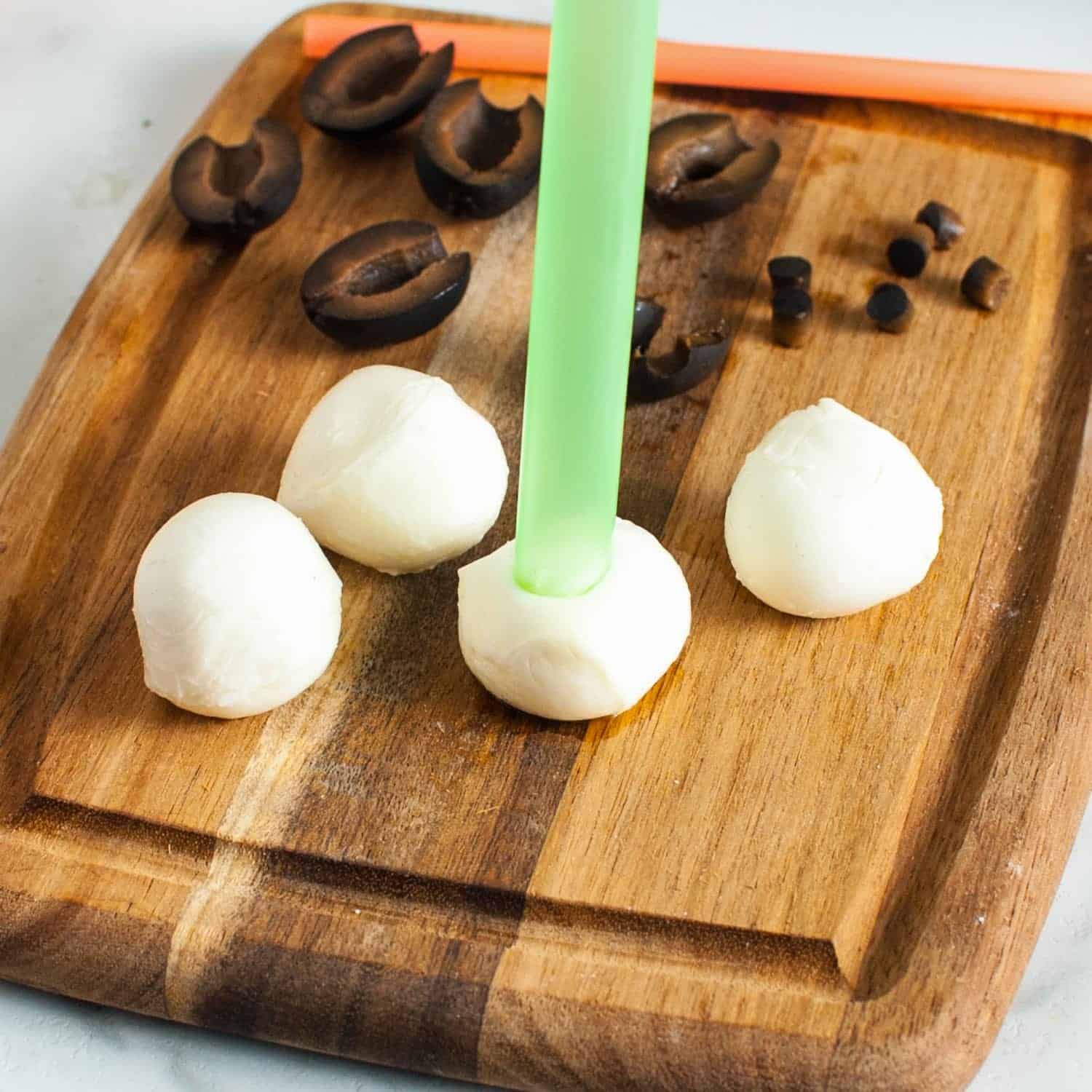 mini mozzarella cheese balls on a wooden cutting board. a wide boba straw is cutting circles out of the centers.