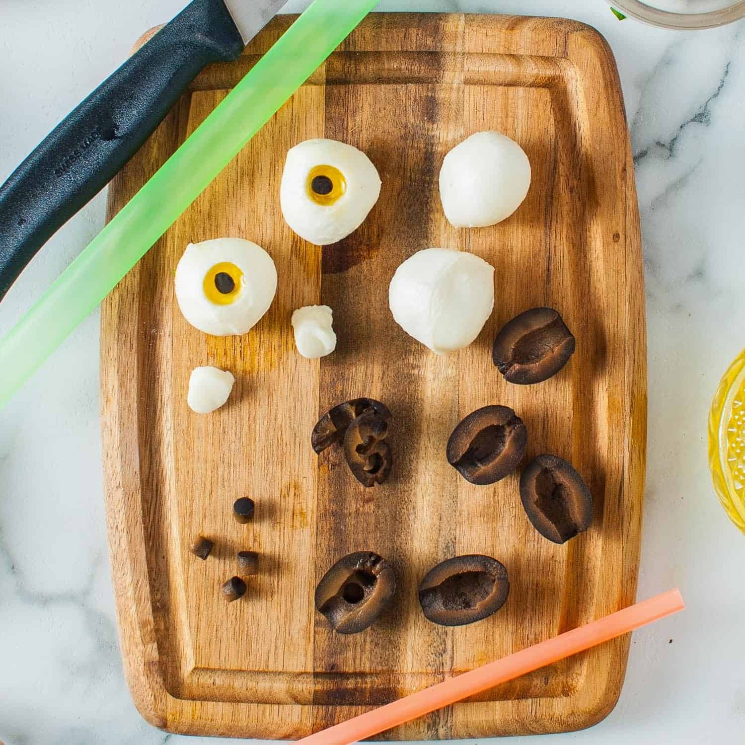 mozzarella eyeballs assembled on a wooden cutting board from small cheese balls, black olive pieces, and olive oil.