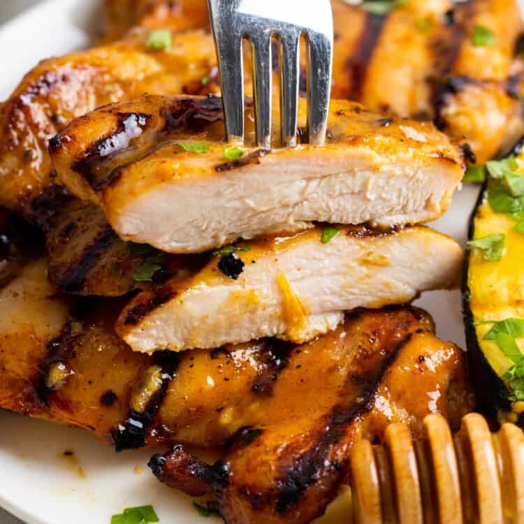 grilled honey mustard chicken on a plate. A piece has been cut in half to show the juicy interior.