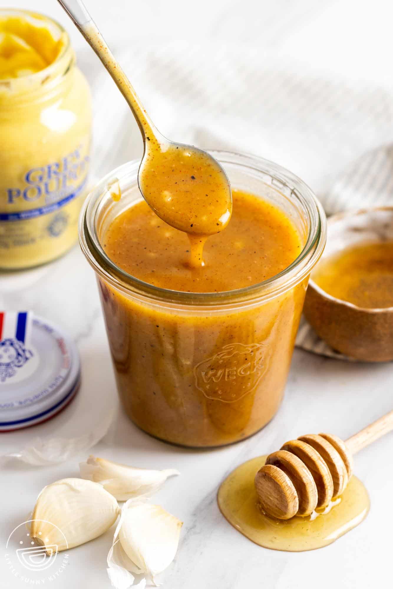 a small glass weck jar of honey mustard marinade next to a jar of grey poupon.