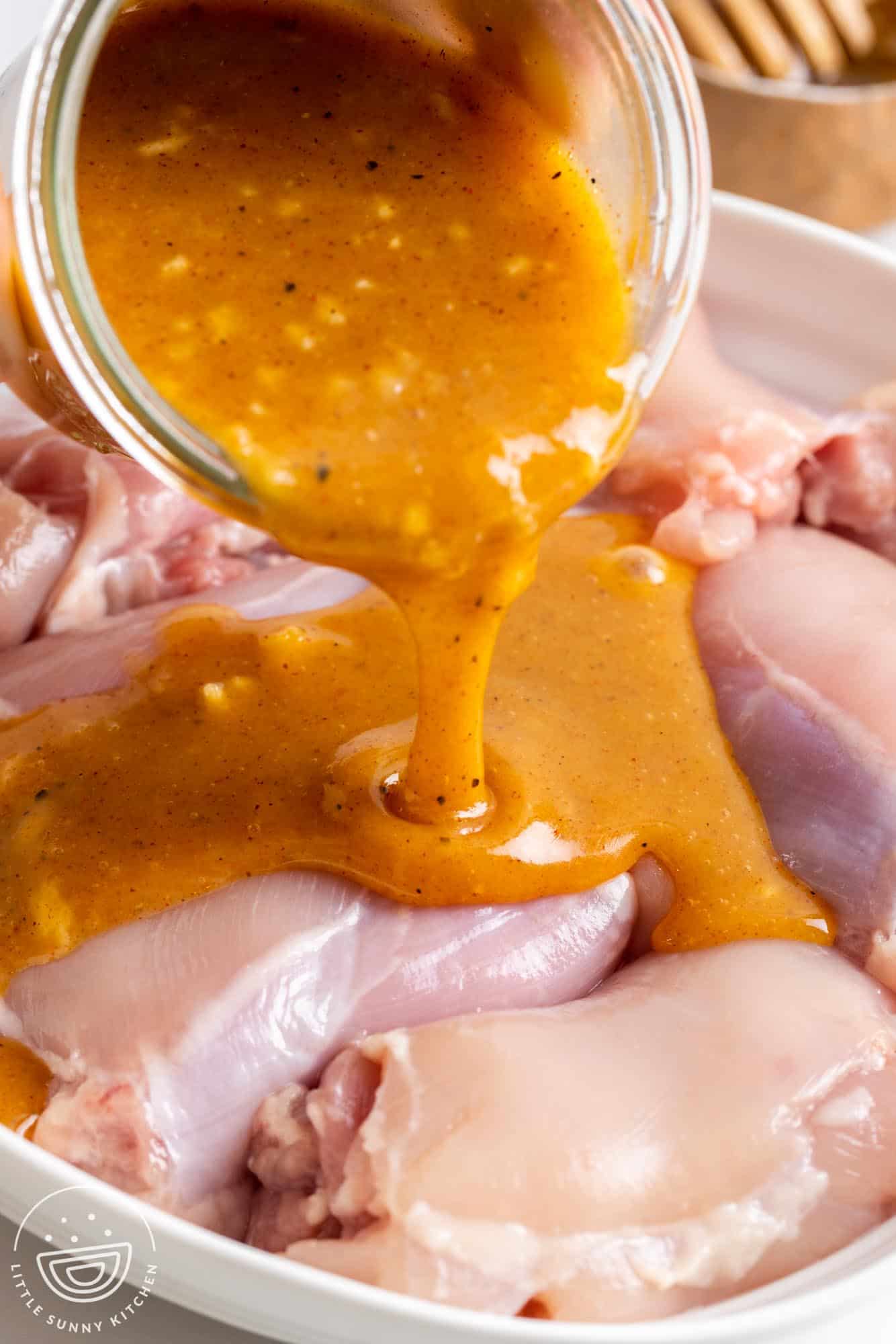 Honey mustard marinade poured over raw boneless skinless chicken thighs.