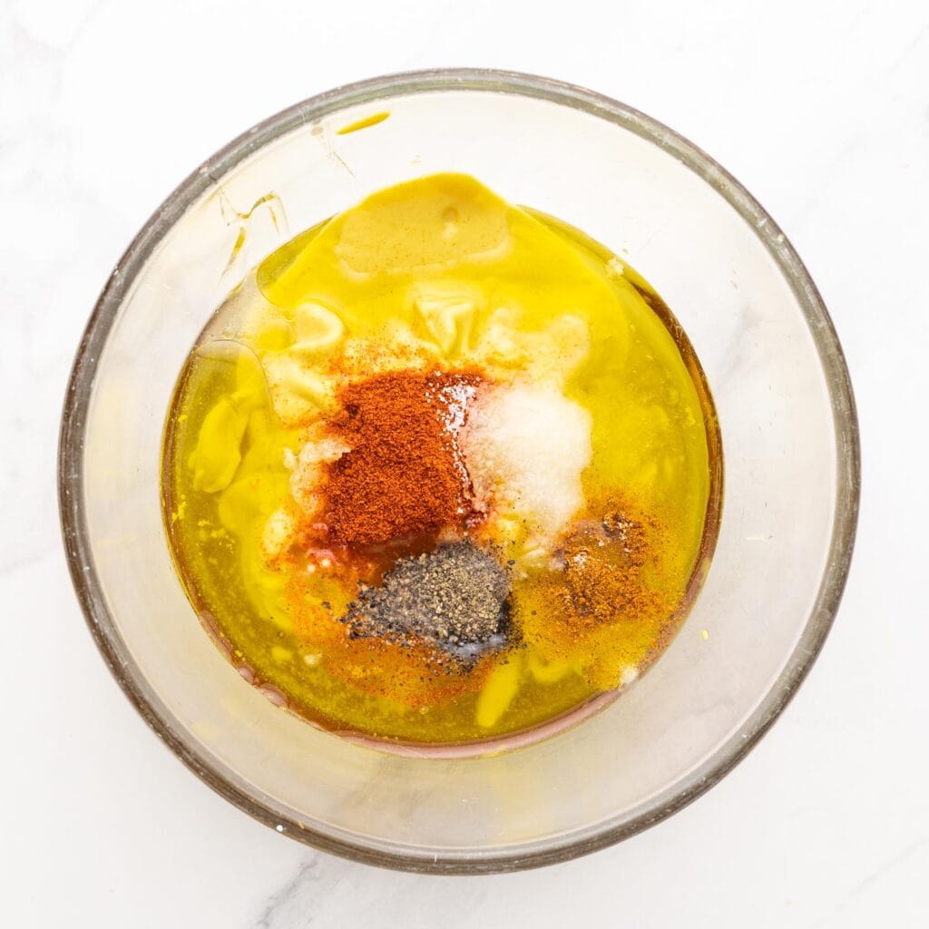 oil, mustard, honey, and seasonings in a glass mixing bowl.