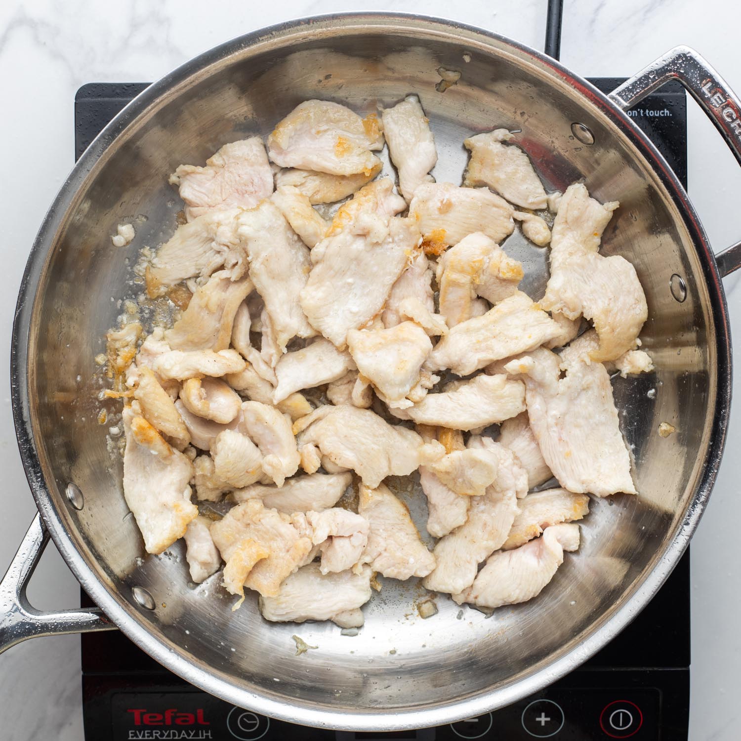 stir fried thin slices of chicken breast in a stainless steel pan.