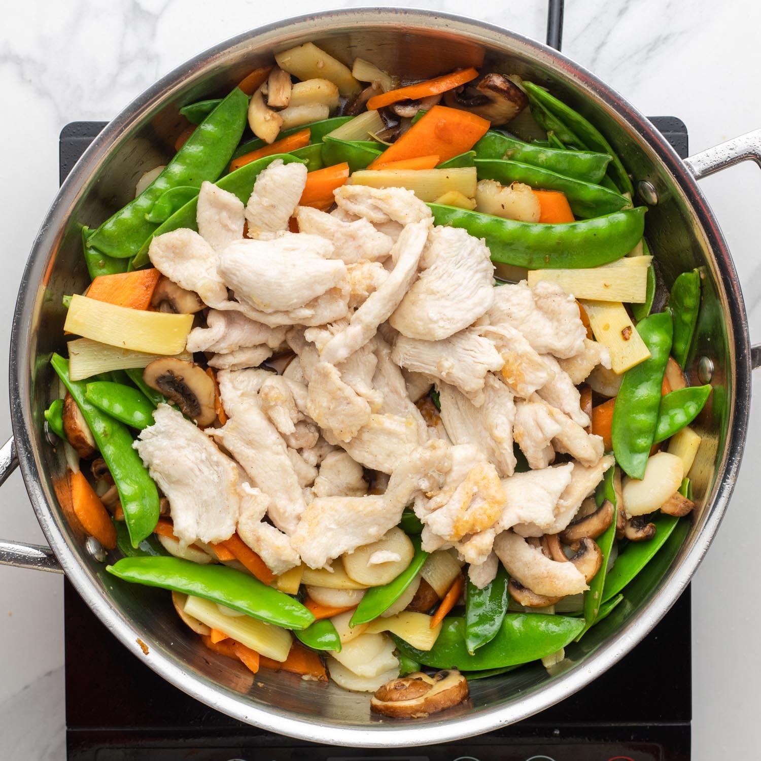 cooked chicken added to stir fried veggies in a skillet.