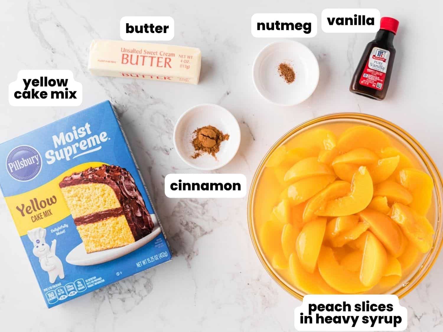 yellow cake mix, canned peaches, butter, cinnamon, nutmeg, and vanilla, arranged on a counter.