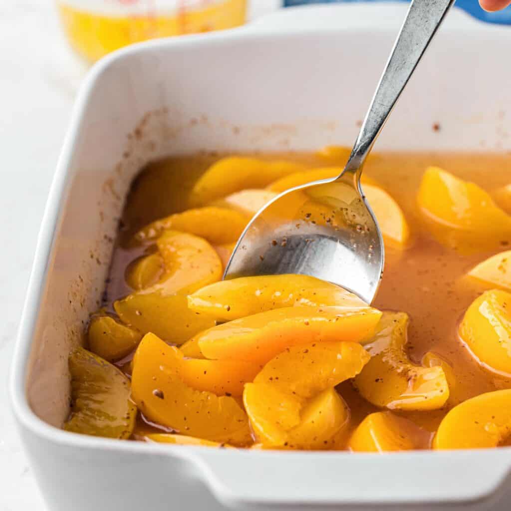 canned peaches with seasonings in a square baking dish.