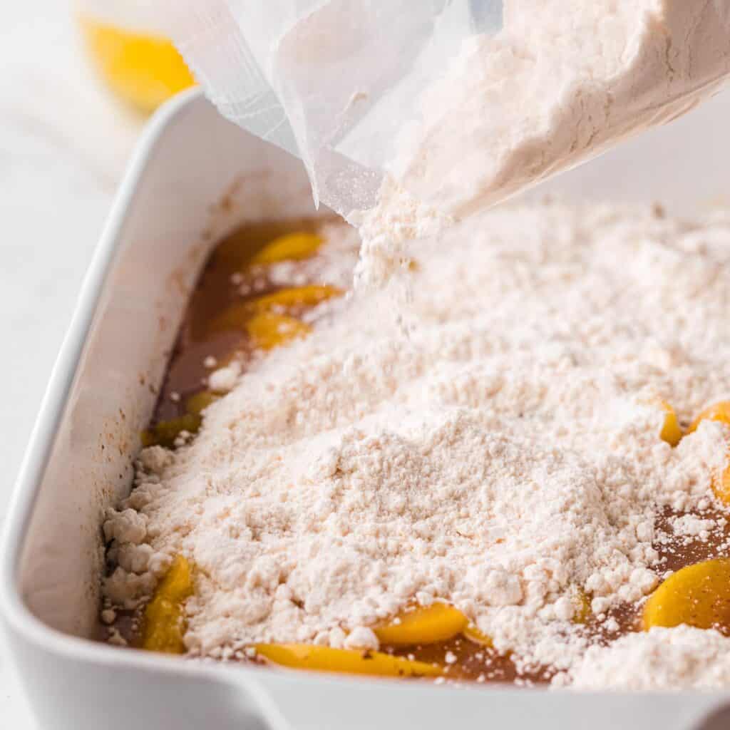 cake mix poured over sliced peaches in a square pan.