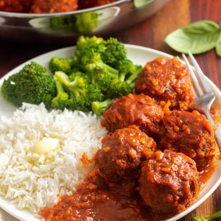 5 porcupine meatballs with tomato sauce on a plate with buttered rice and broccoli.