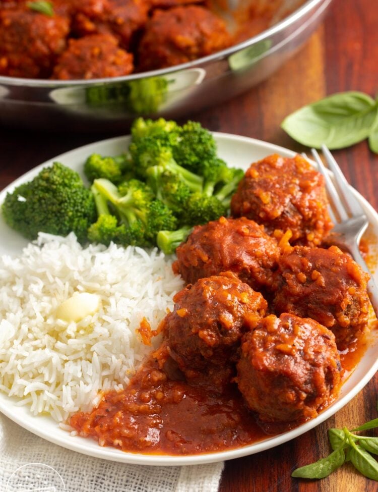 5 porcupine meatballs with tomato sauce on a plate with buttered rice and broccoli.