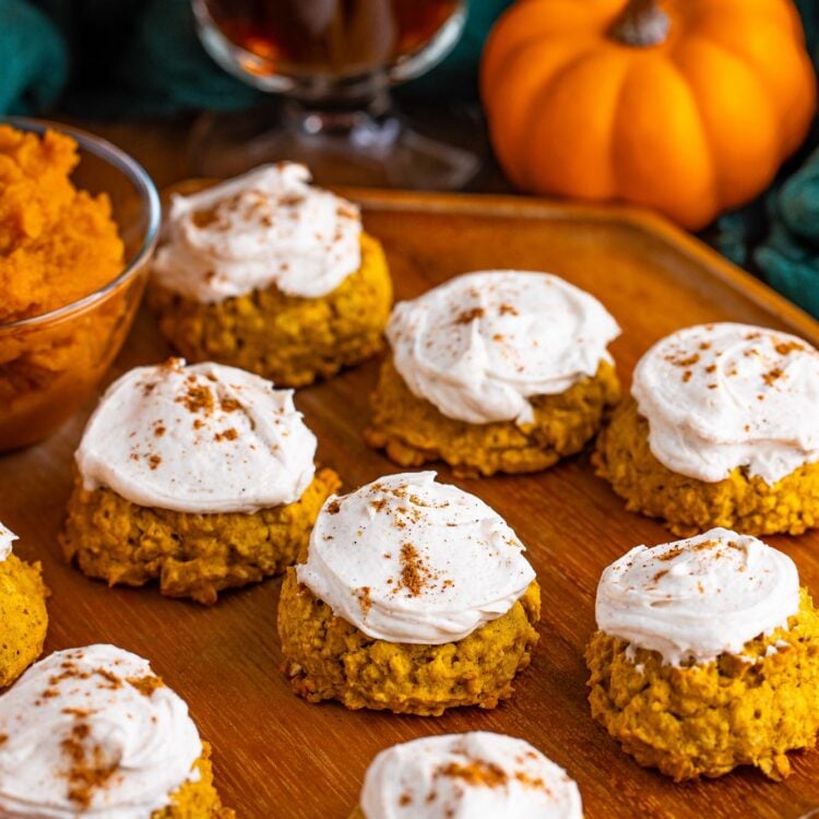 a wooden platter holding 9 thick pumpkin oatmeal cookies topped with pumpkin spice buttercream.