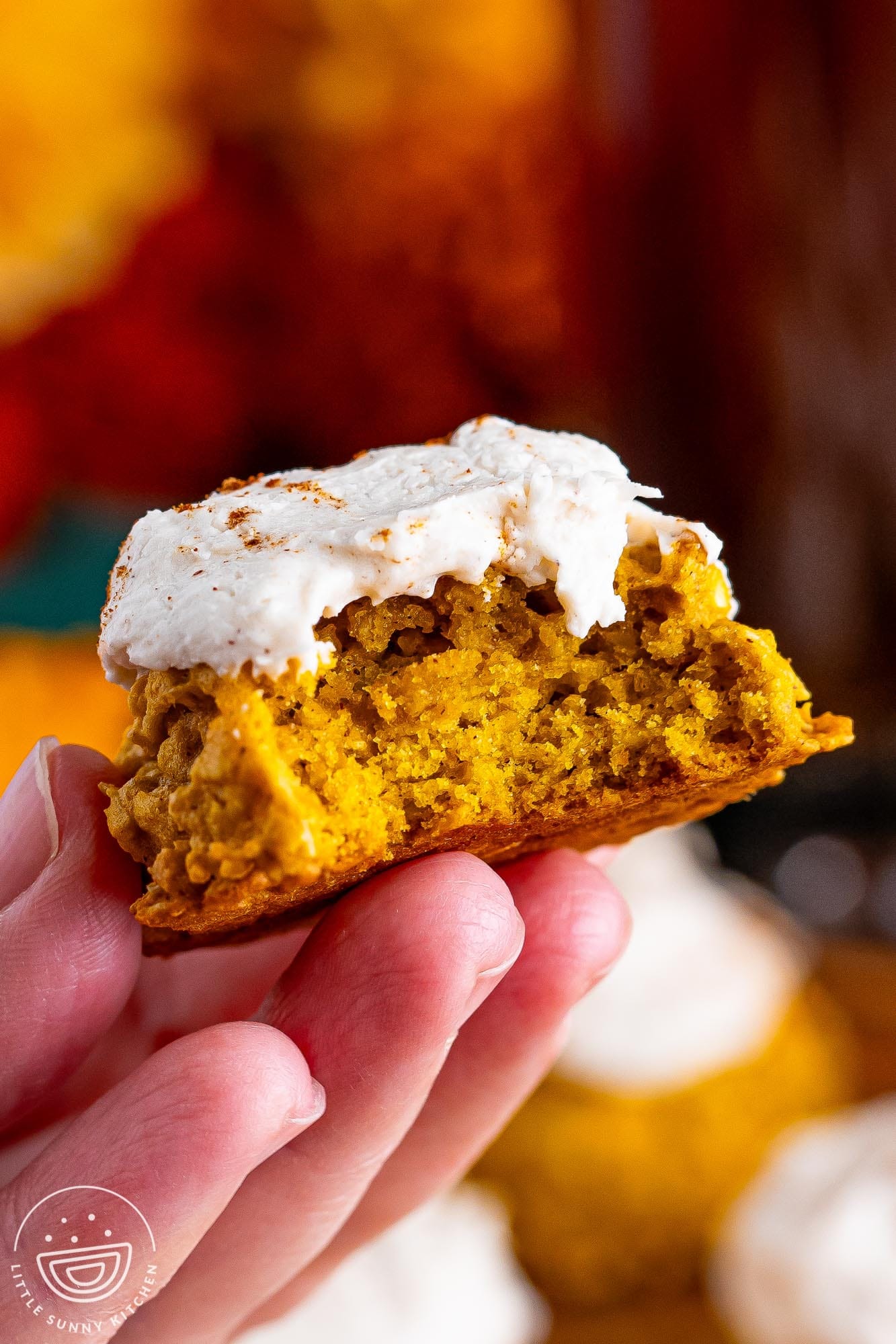 a hand holding a soft, thick pumpkin oatmeal cookie with frosting. A bite has been taken to show the texture.