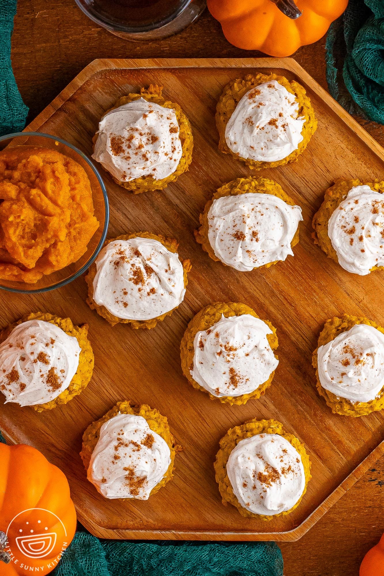 overhead view of an octagon shaped wooden tray holding 10 frosted pumpkin cookies and small bowl of pumpkin puree.