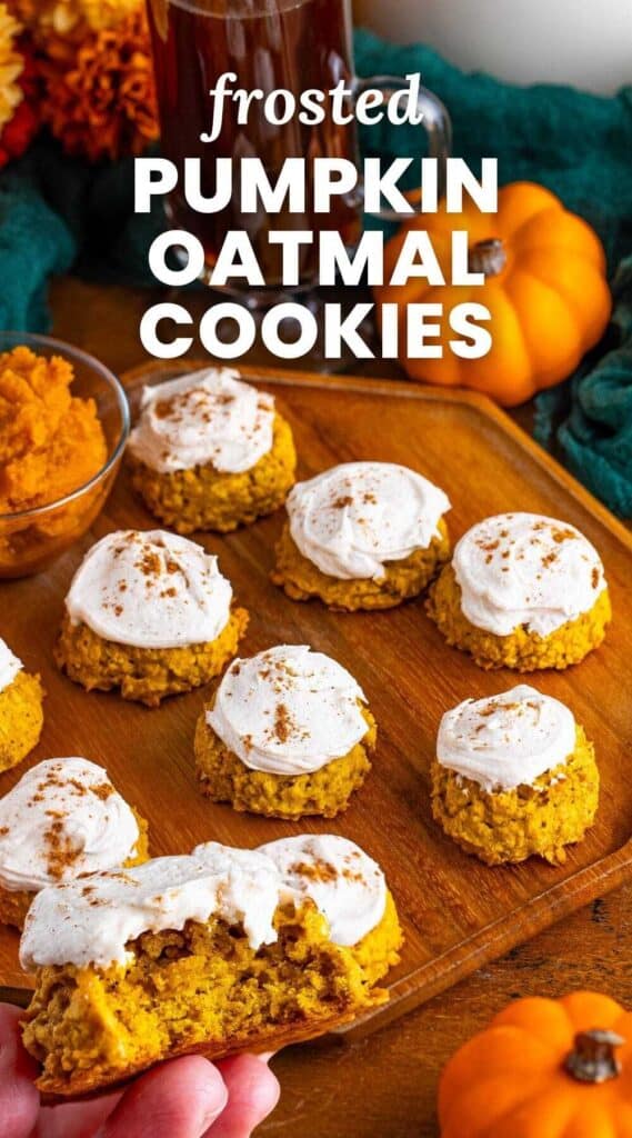 a wooden board of frosted pumpkin cookies. A hand is holding one up. Text overlay says "frosted pumpkin oatmeal cookies"