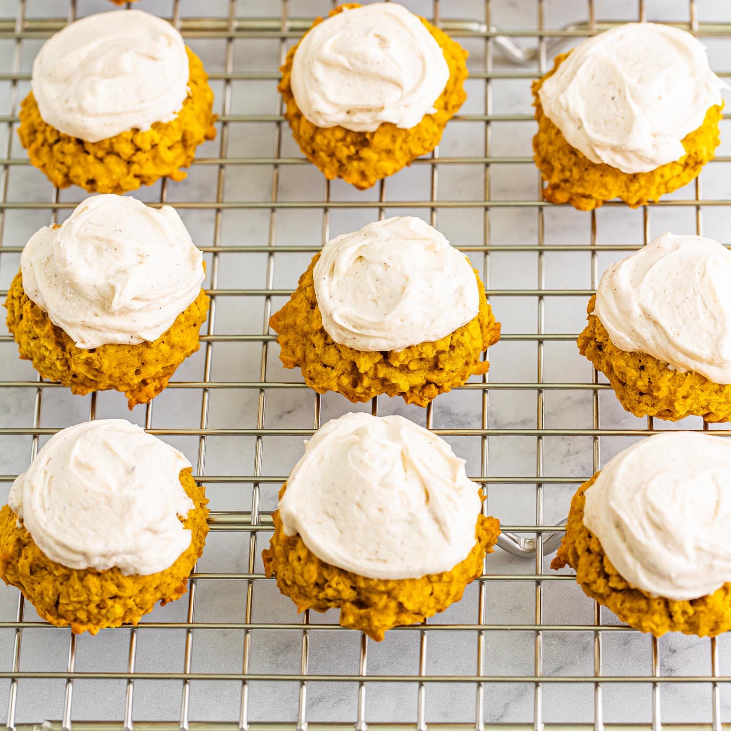 9 pumpkin oatmeal cookies with frosting on a wire rack.