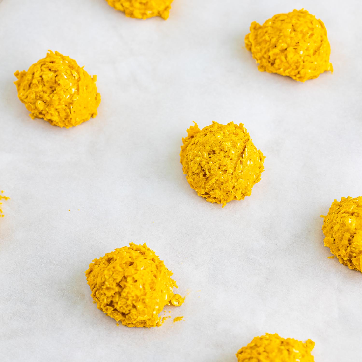 pumpkin oat cookie dough in balls on parchment paper.