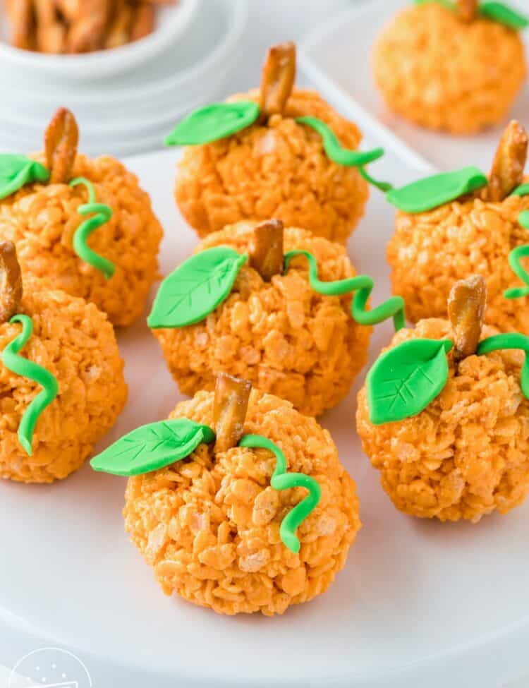 7 pumpkin rice krispie treats on a white cake pedestal.