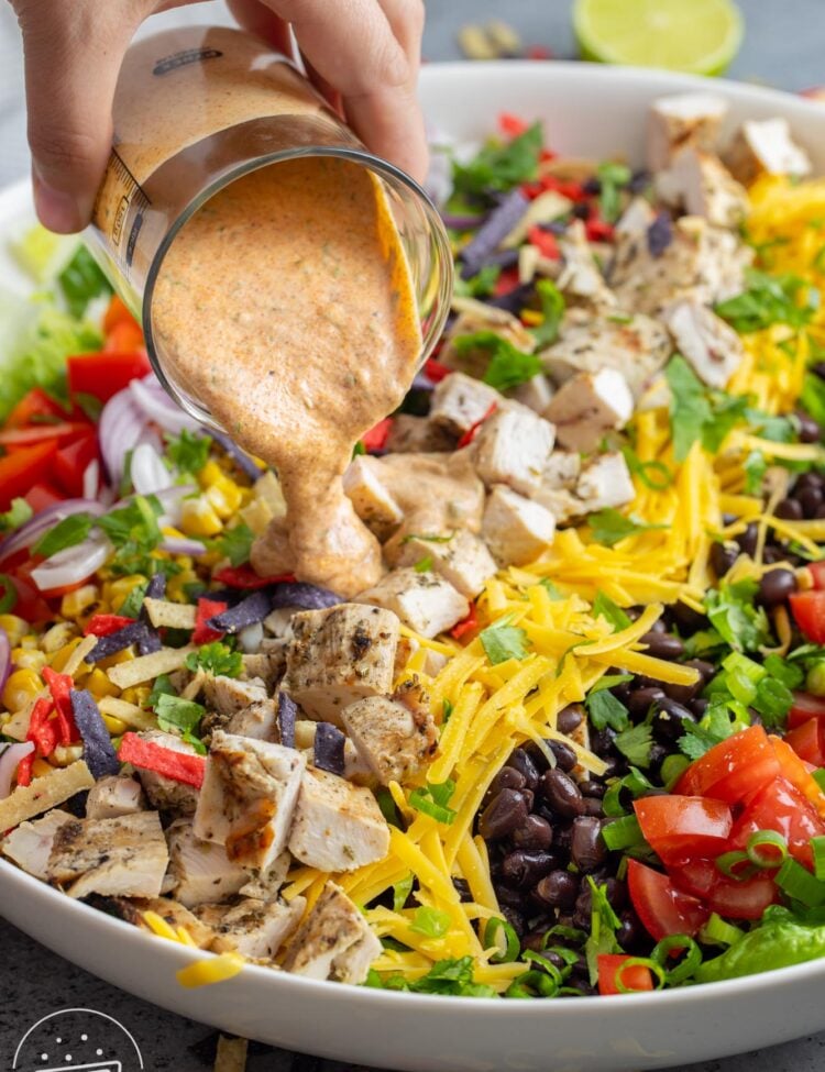 Tex mex chicken salad in a large bowl, and tex mex ranch being poured on top