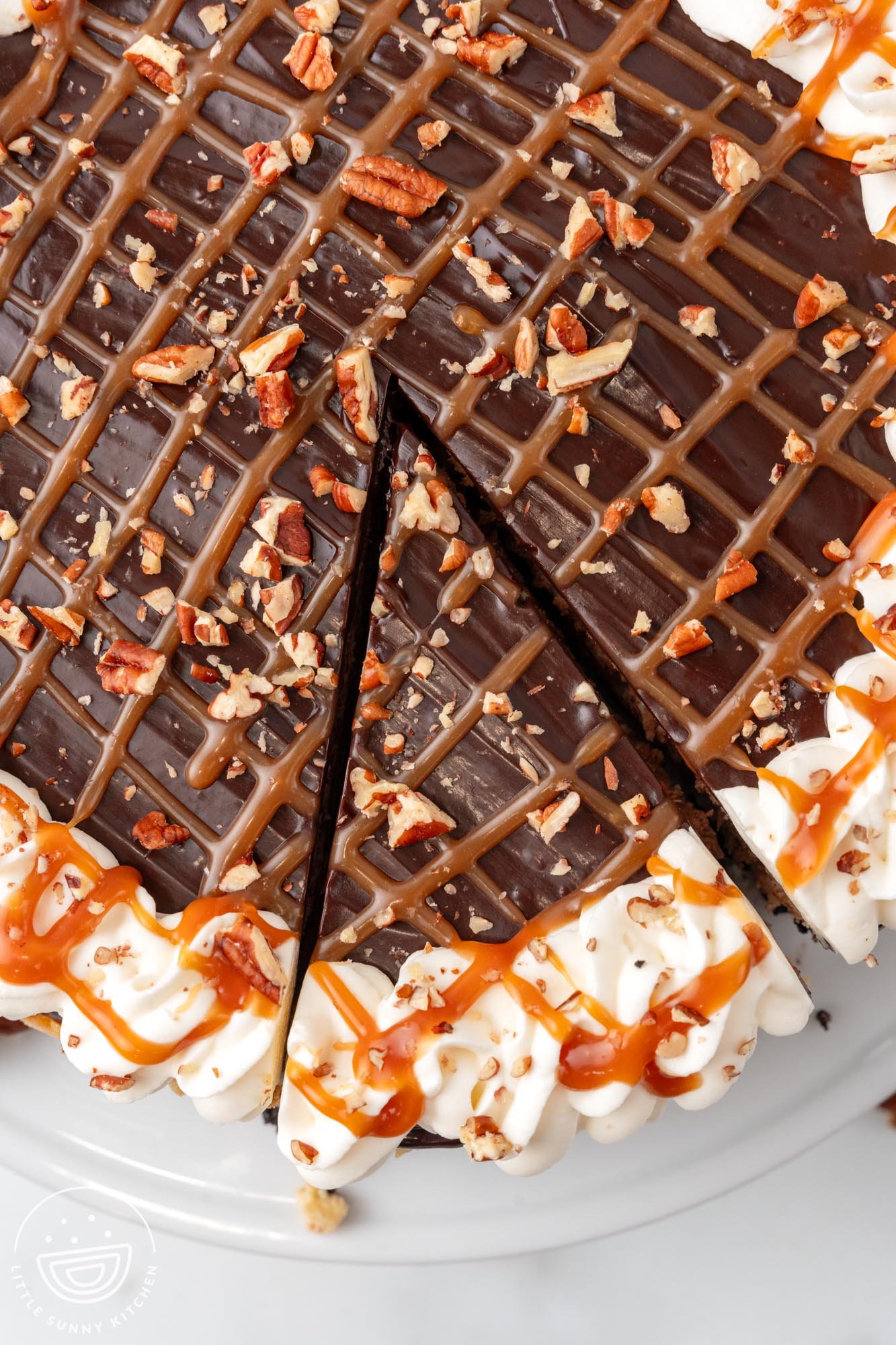 overhead view of a cheesecake topped with chocolate, caramel, and pecans. The edge is decorated with whipped cream.