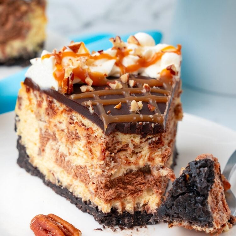 a slice of swirled turtle cheesecake on a plate. A fork has taken a bite from the tip of the slice.