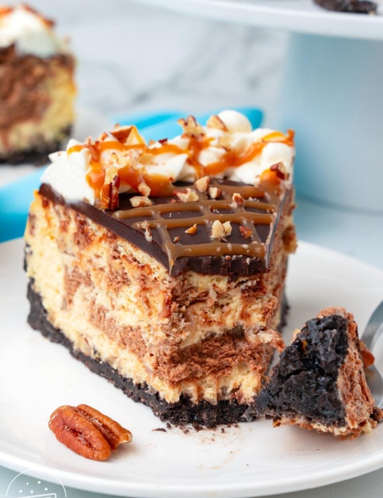 a slice of swirled turtle cheesecake on a plate. A fork has taken a bite from the tip of the slice.