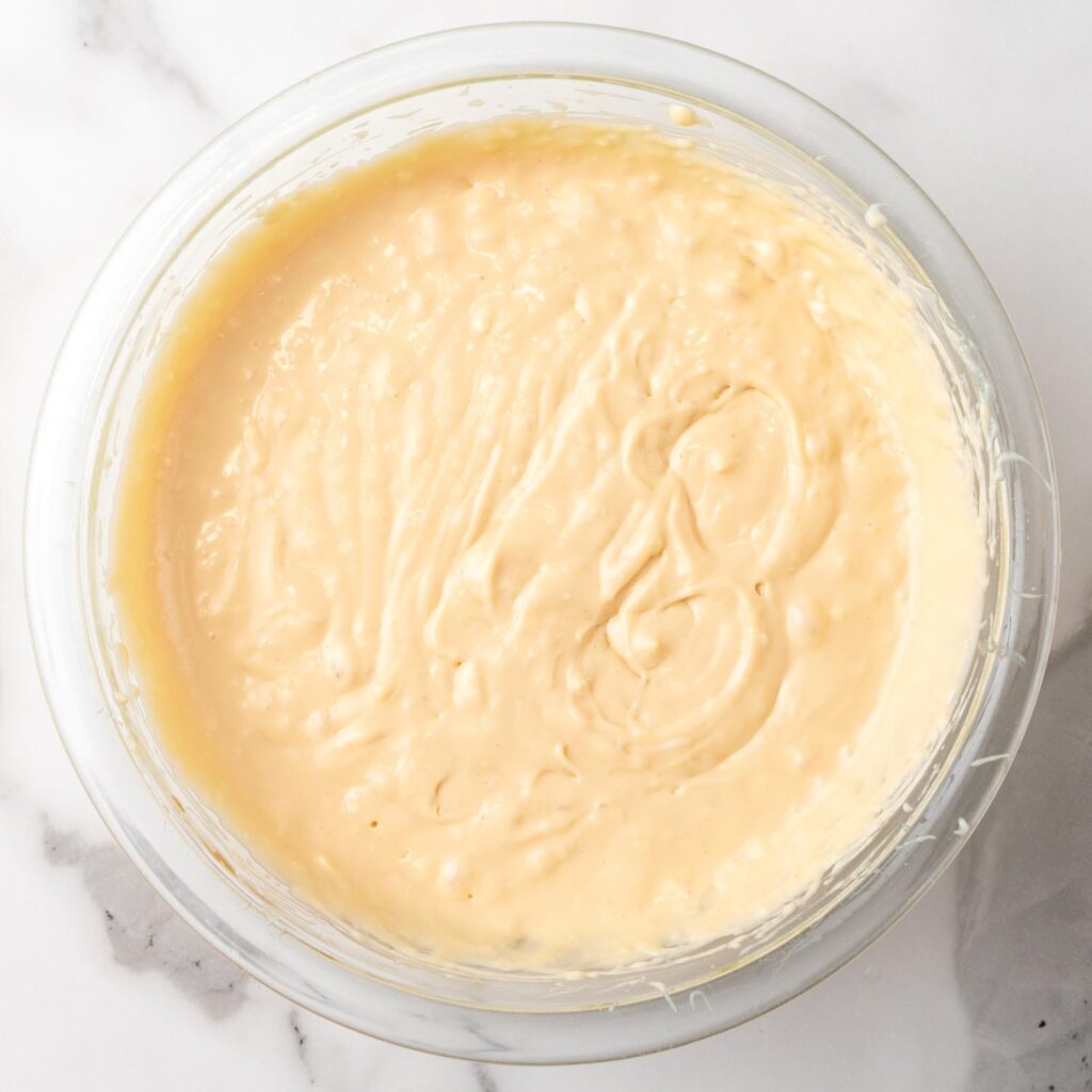 Caramel cheesecake filling in a glass mixing bowl.