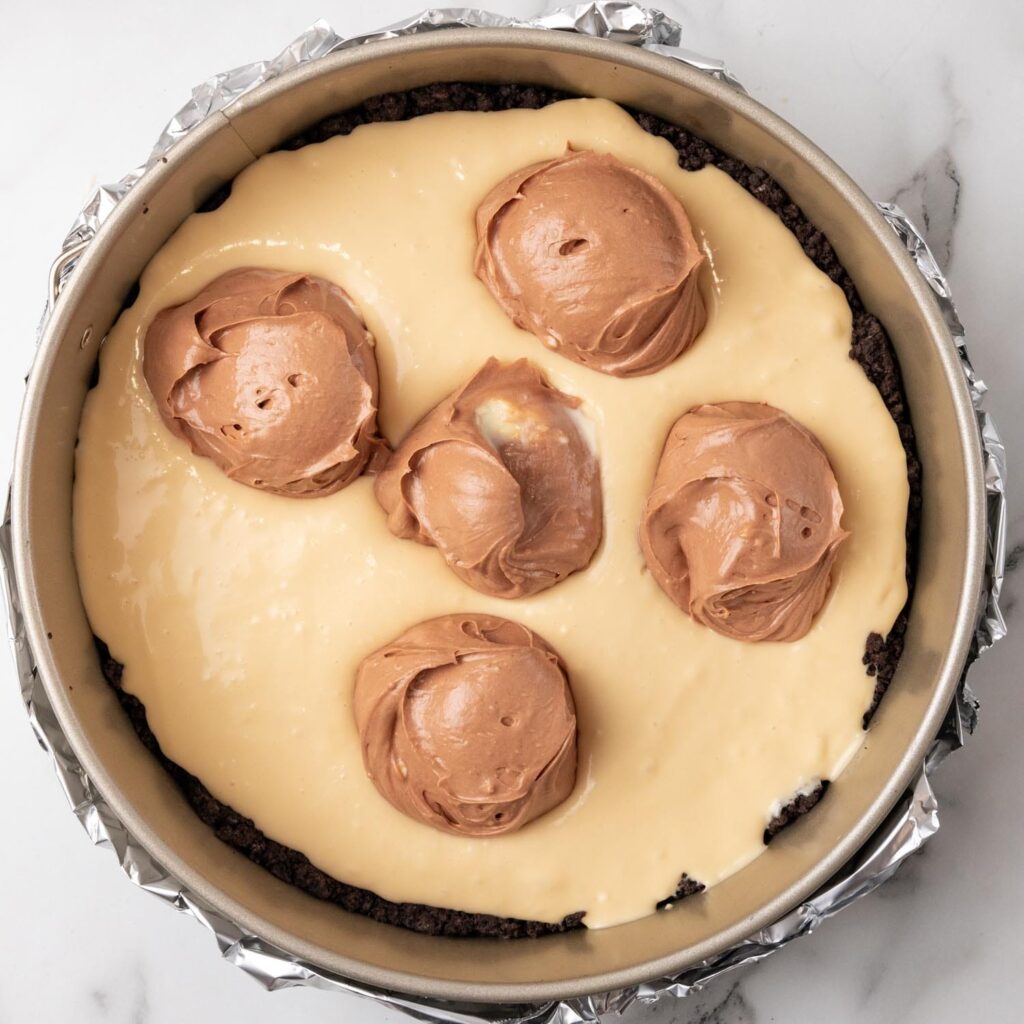 Caramel cheesecake filling added to a crust. Chocolate filling is scooped onto it in 5 portions.