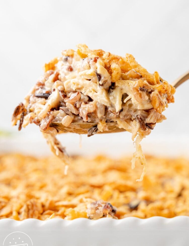 a scoop of chicken and wild rice casserole held up over the baking dish, viewed from the side.