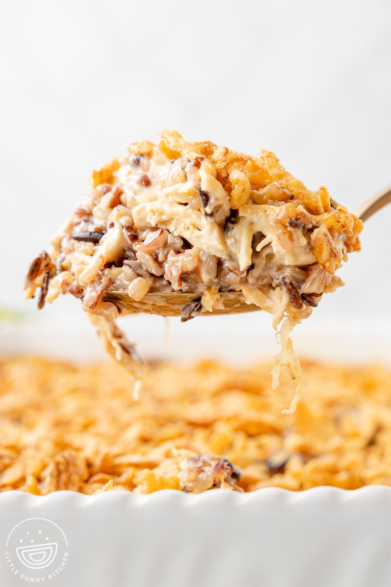 a scoop of chicken and wild rice casserole held up over the baking dish, viewed from the side.