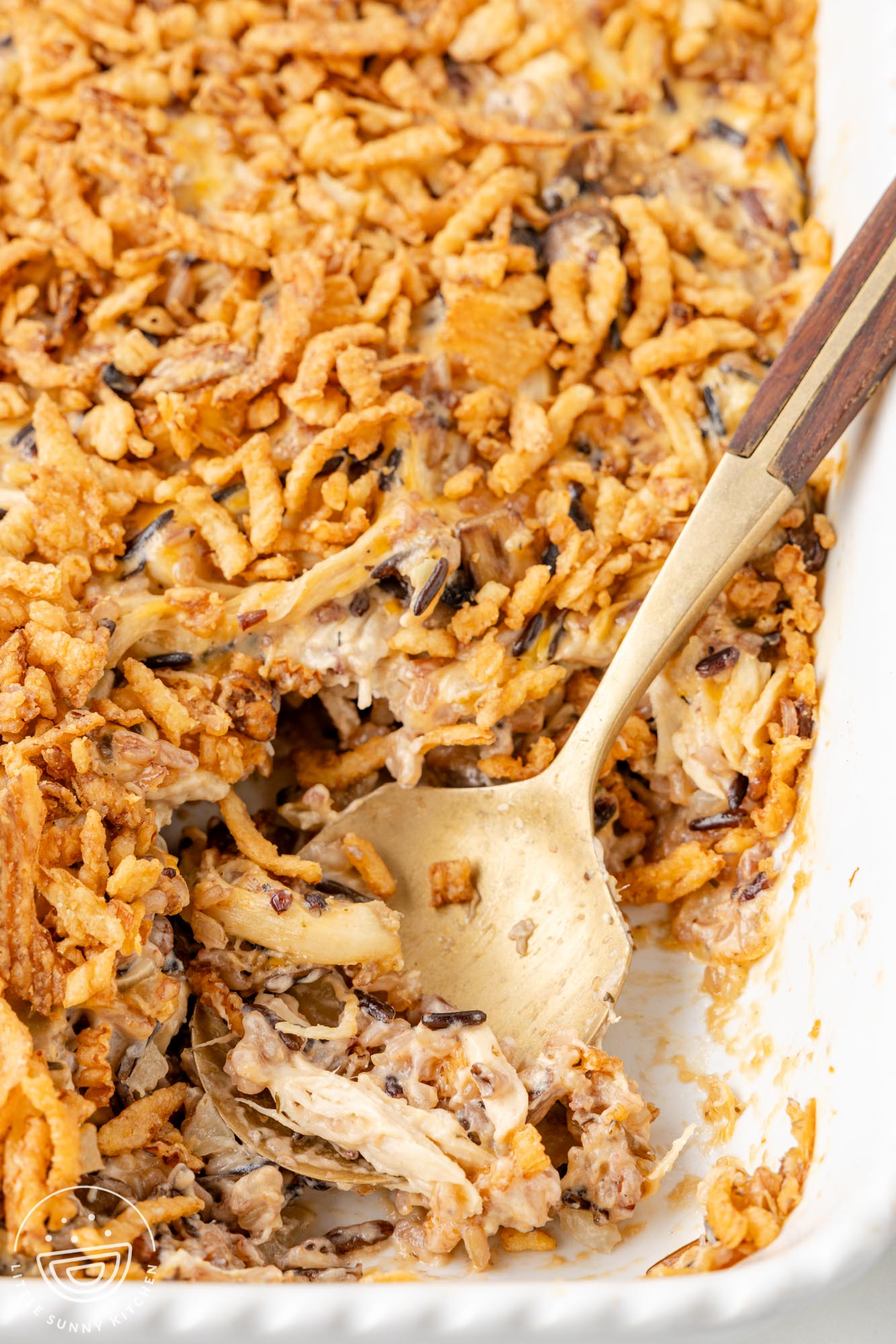 a white baking dish of chicken casserole with wild rice, topped with frenchs onions. A large spoon has taken a serving from the front corner.