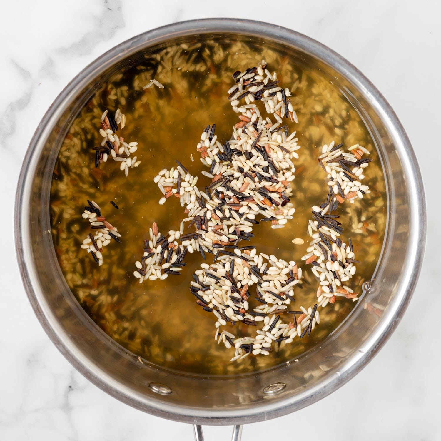 wild rice cooking in broth in a metal saucepan.