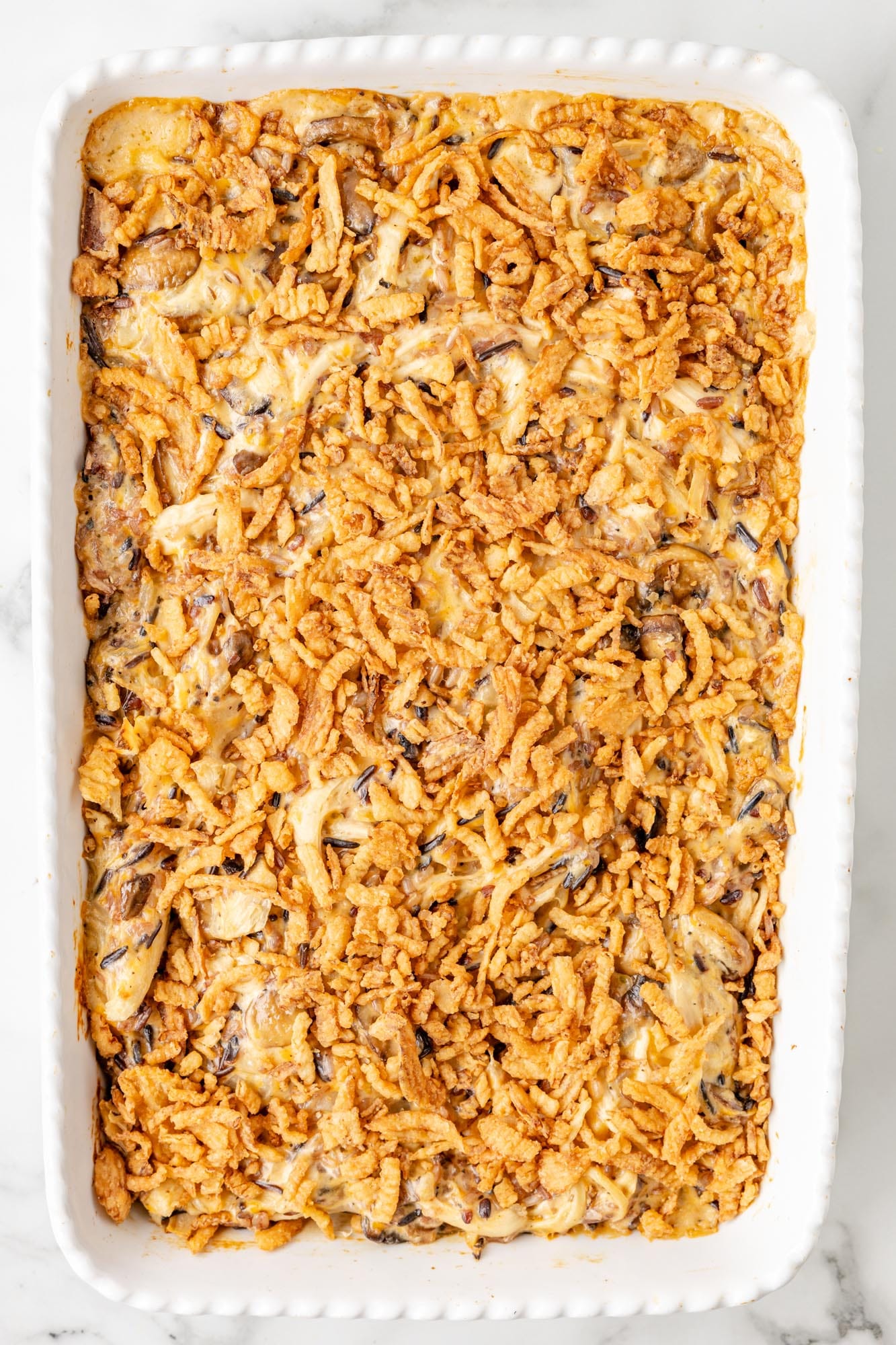 a rectangular white baking dish holding a crispy onion topped casserole of chicken and wild rice.