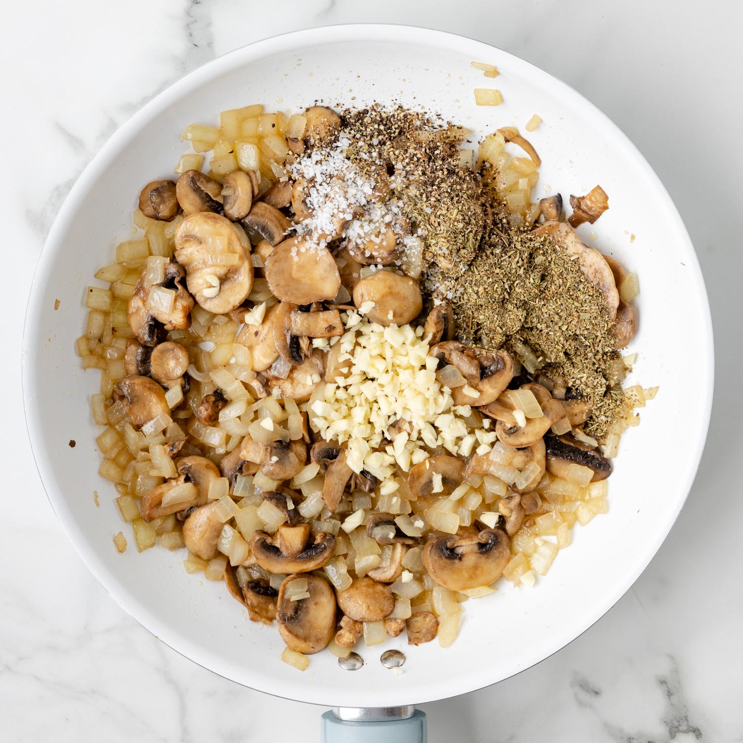 a white enameled skillet of sauteed onions and mushrooms with minced garlic and seasonings added.