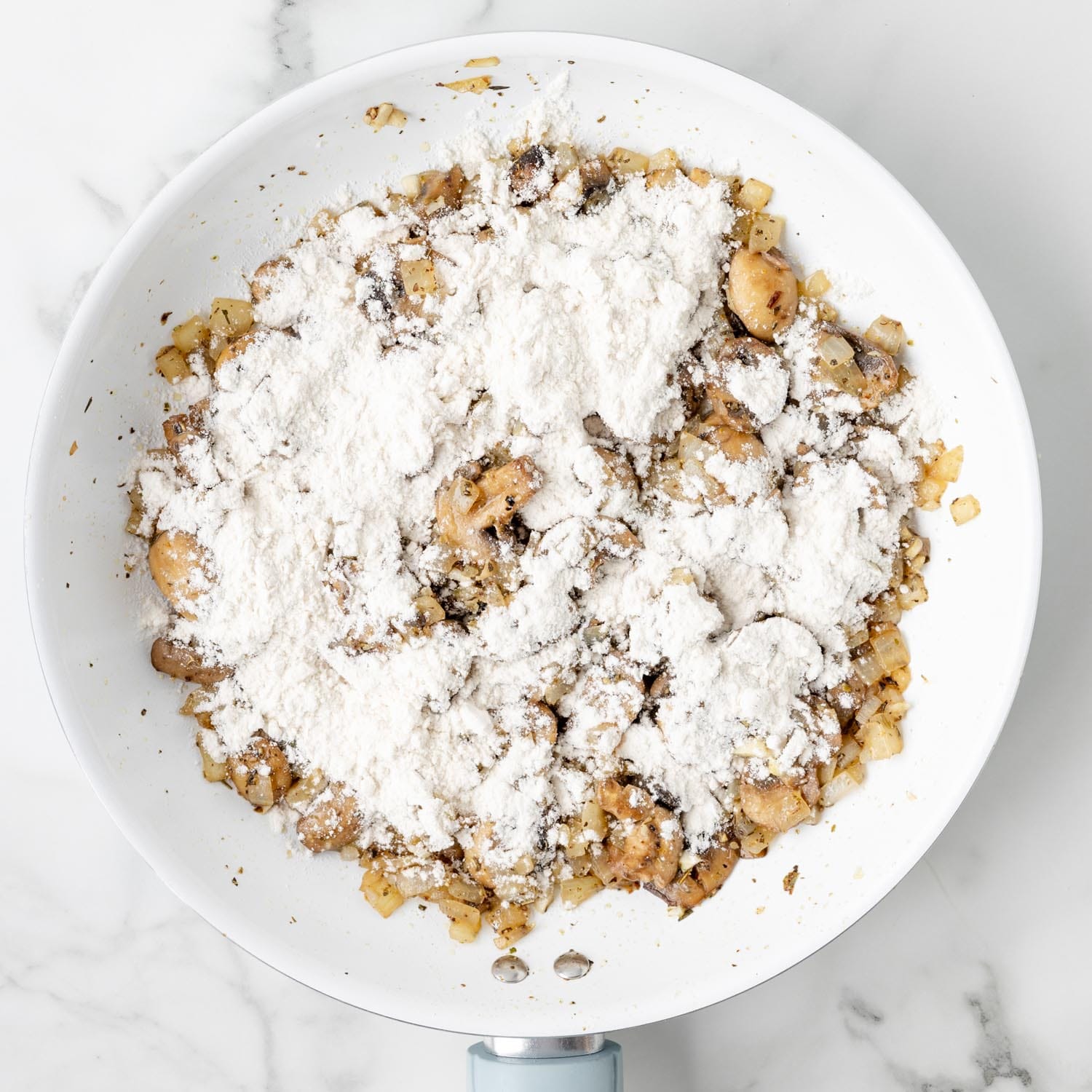 flour added to cooked mushrooms and onions in a white skillet.