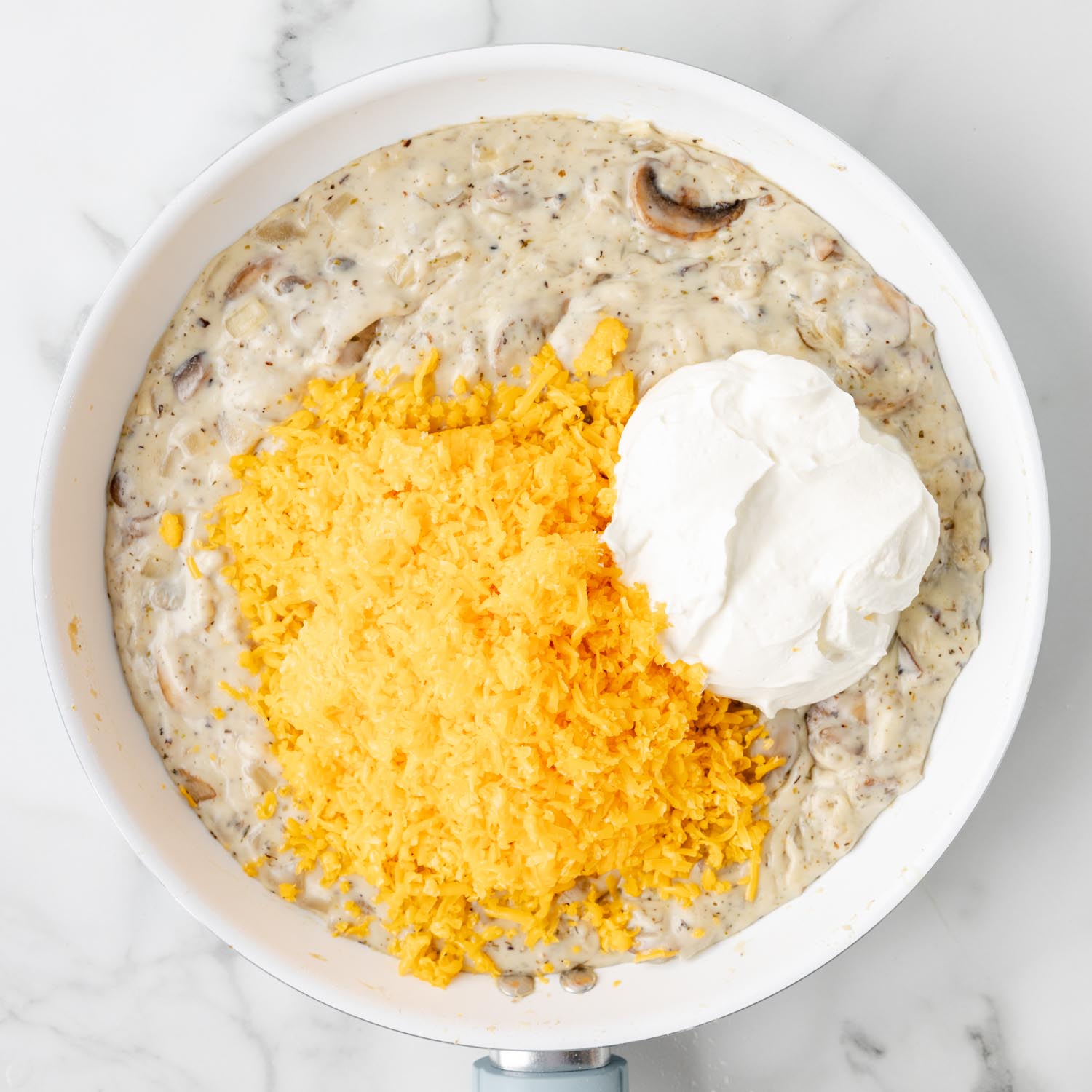 sour cream and shredded cheddar cheese added to mushroom sauce in a white enameled skillet.