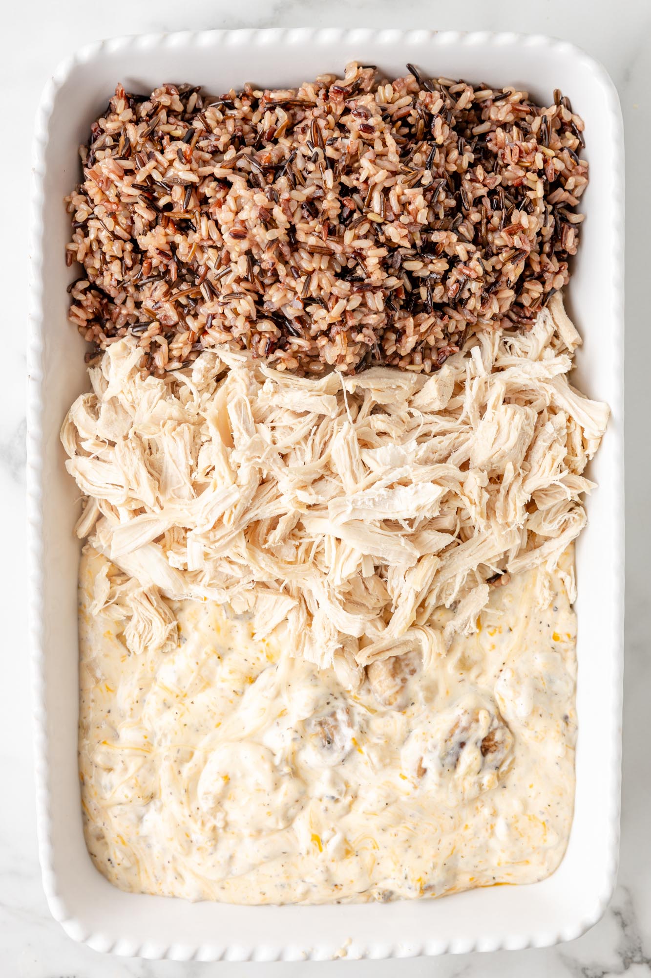 creamy mushroom sauce, shredded chicken, and cooked wild rice added to a baking dish.