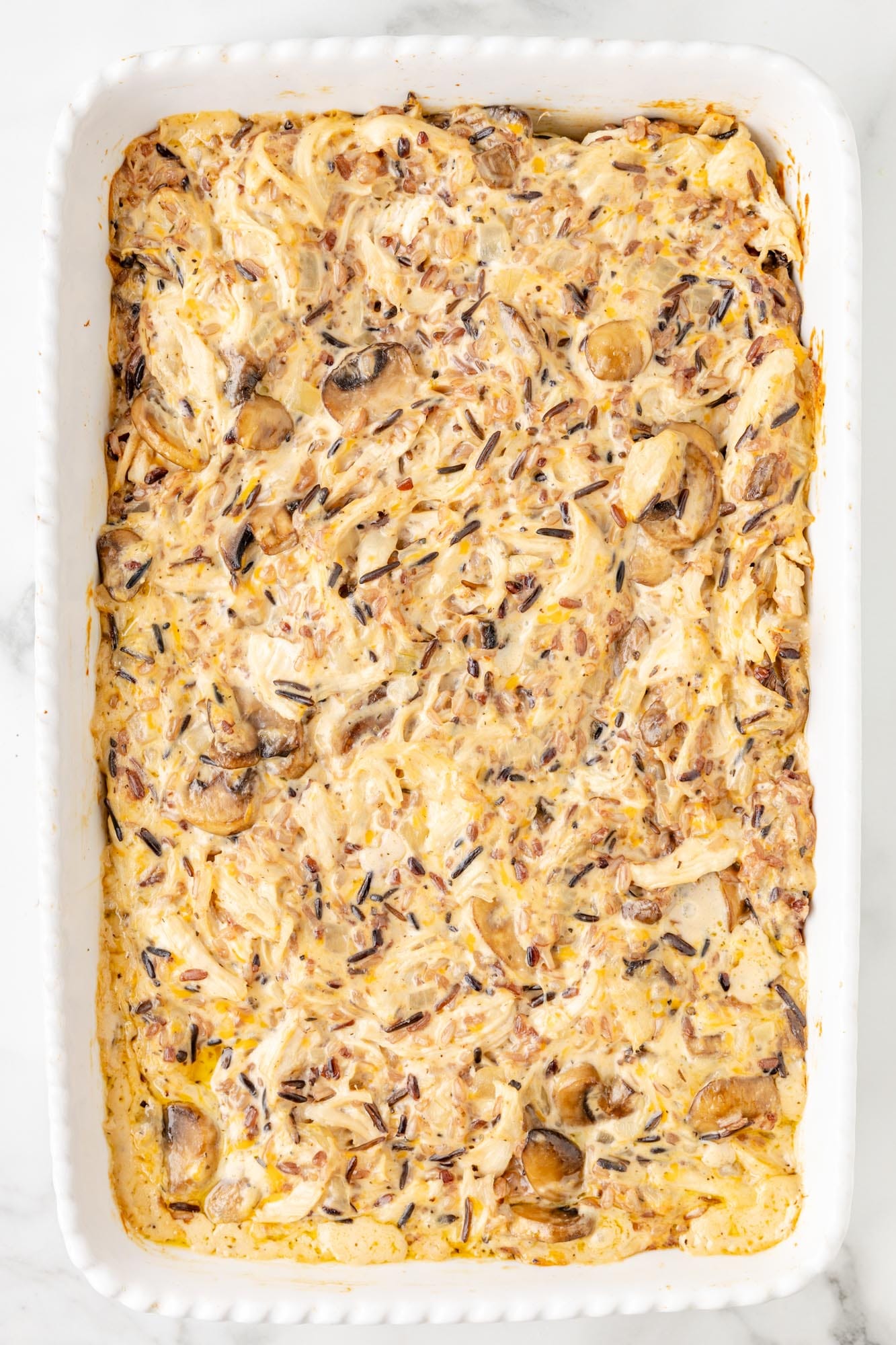 baked creamy mixture of shredded chicken, mushrooms, wild rice in a rectangular white baking dish.