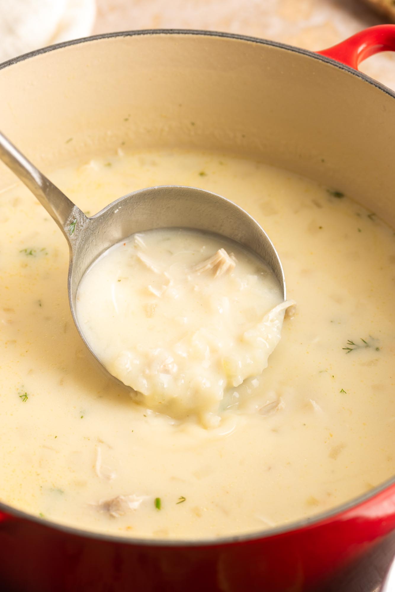 greek lemon chicken soup in a red dutch oven. A ladle is holding some uip to show the creamy rice texture and tender shredded chicken.