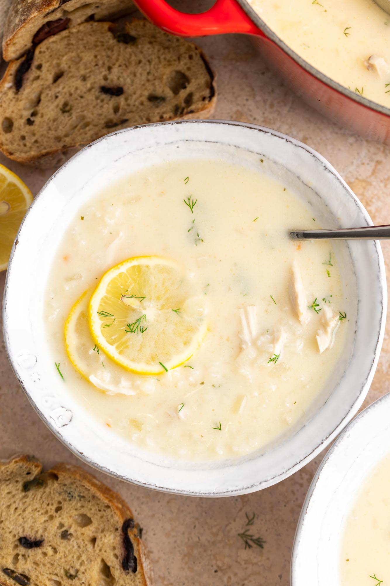 avgolemono soup in a white ceramic bowl, garnished with two lemon wheels, viewed from overhead.