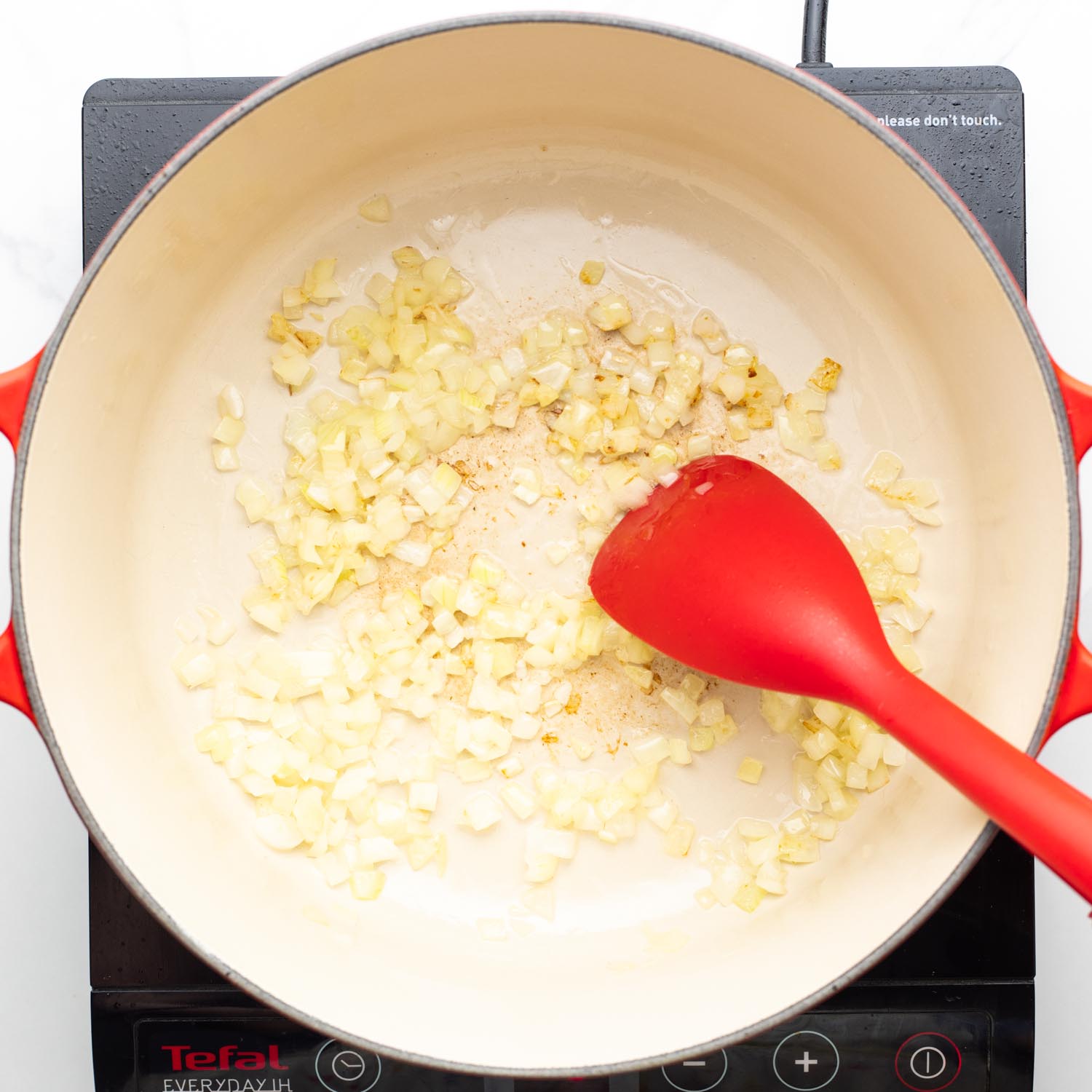 onion and garlic sauteed in a dutch oven with a red spatula.