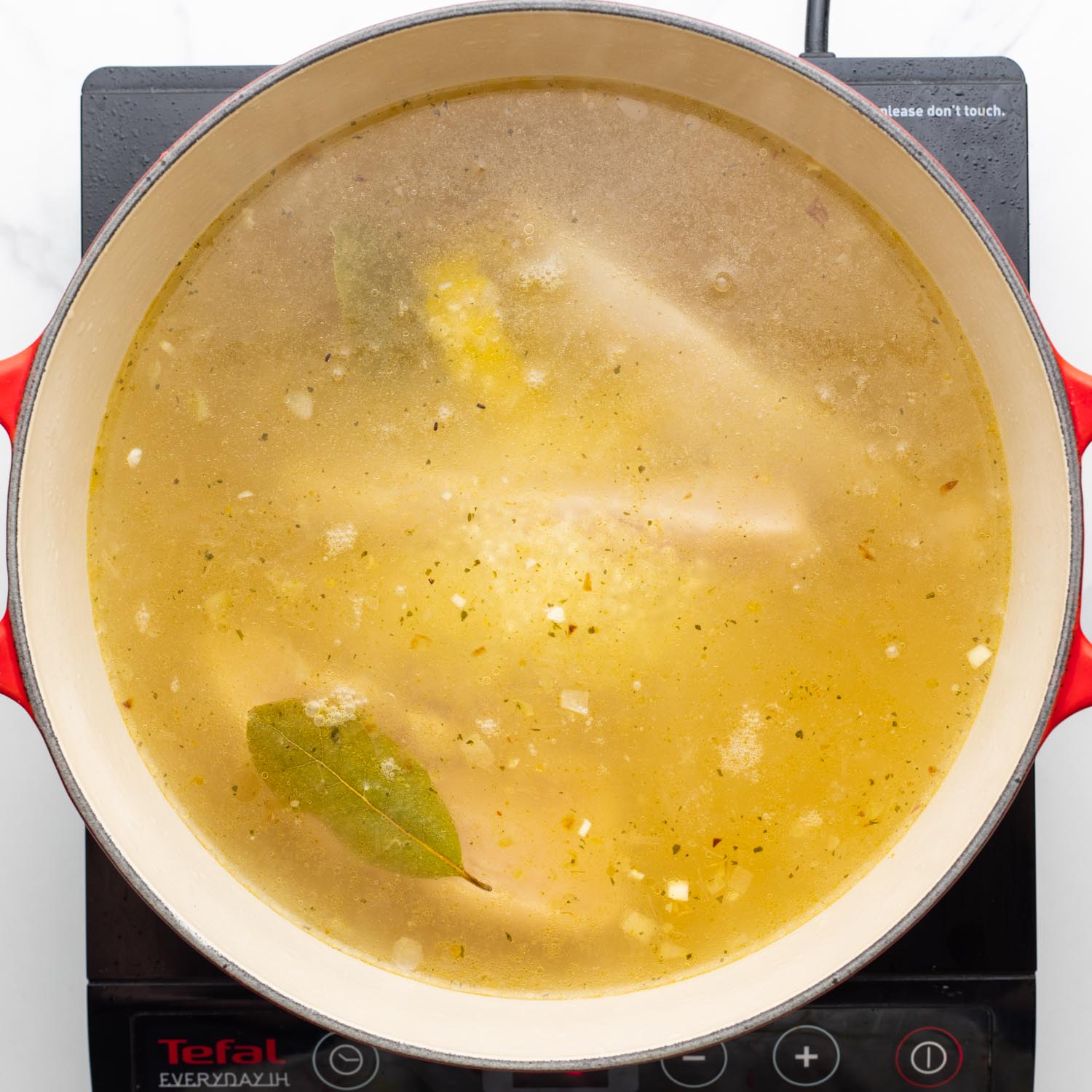 chicken simmering in broth with lemons and bay leaves.