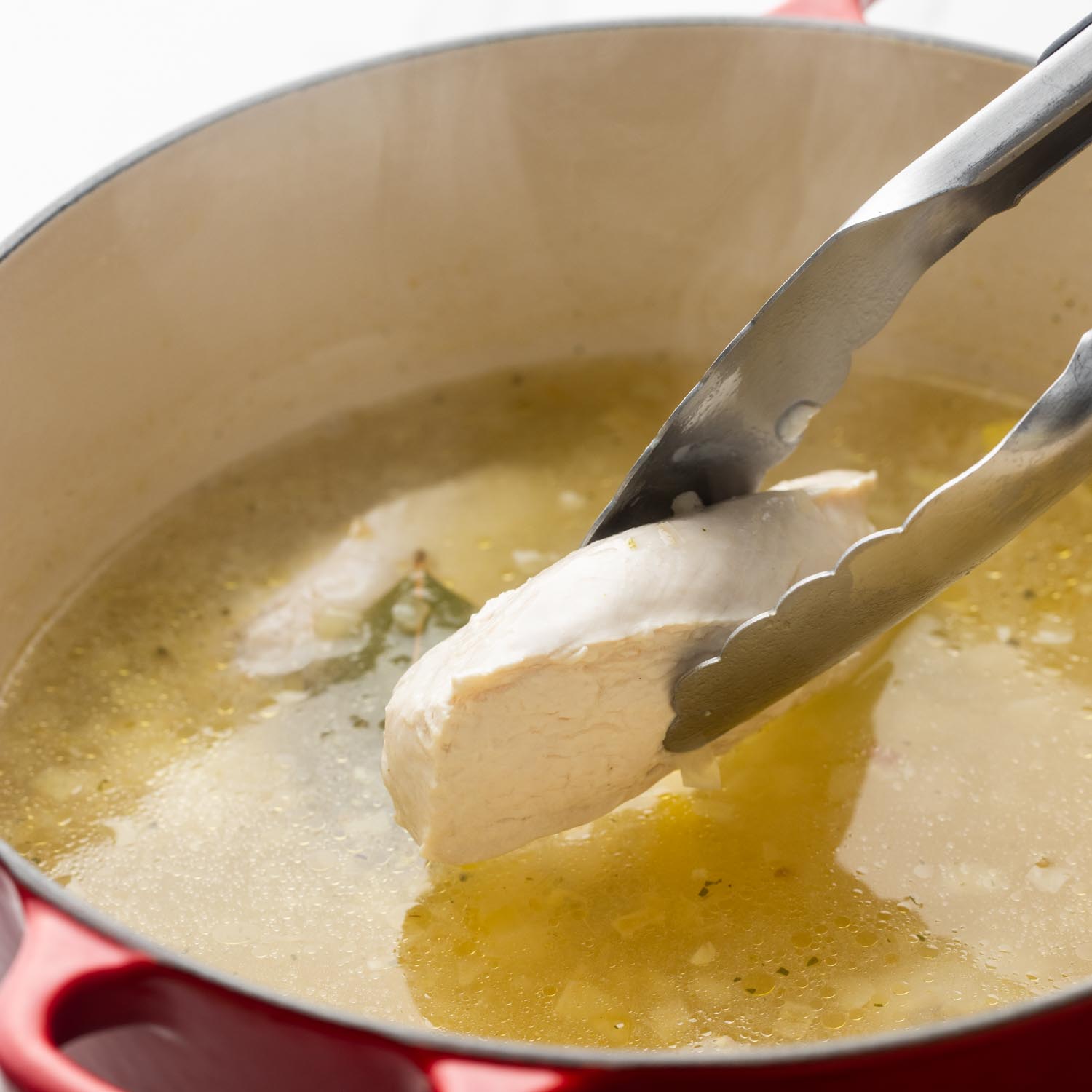 poached chicken breast slices removed from lemony chicken broth with tongs.