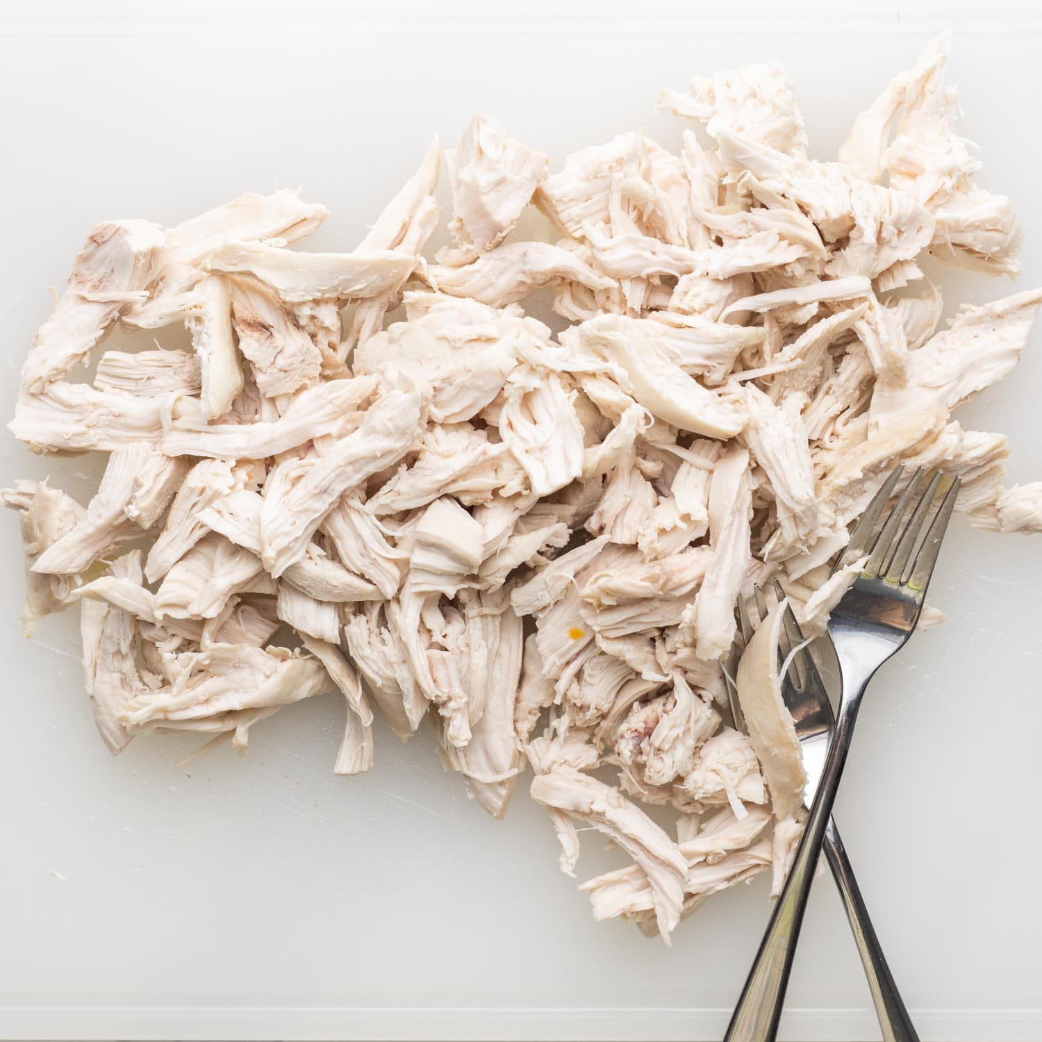 shredded chicken breast meat on a cutting board with two forks.