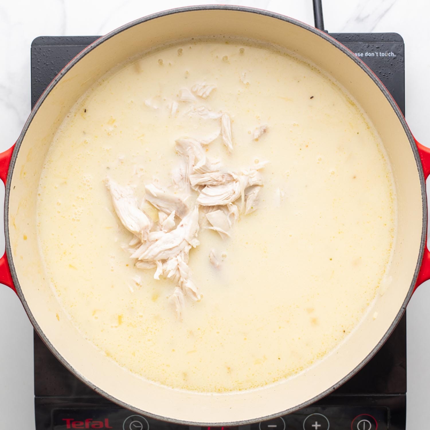 shredded chicken added to creamy lemon rice soup in a dutch oven.