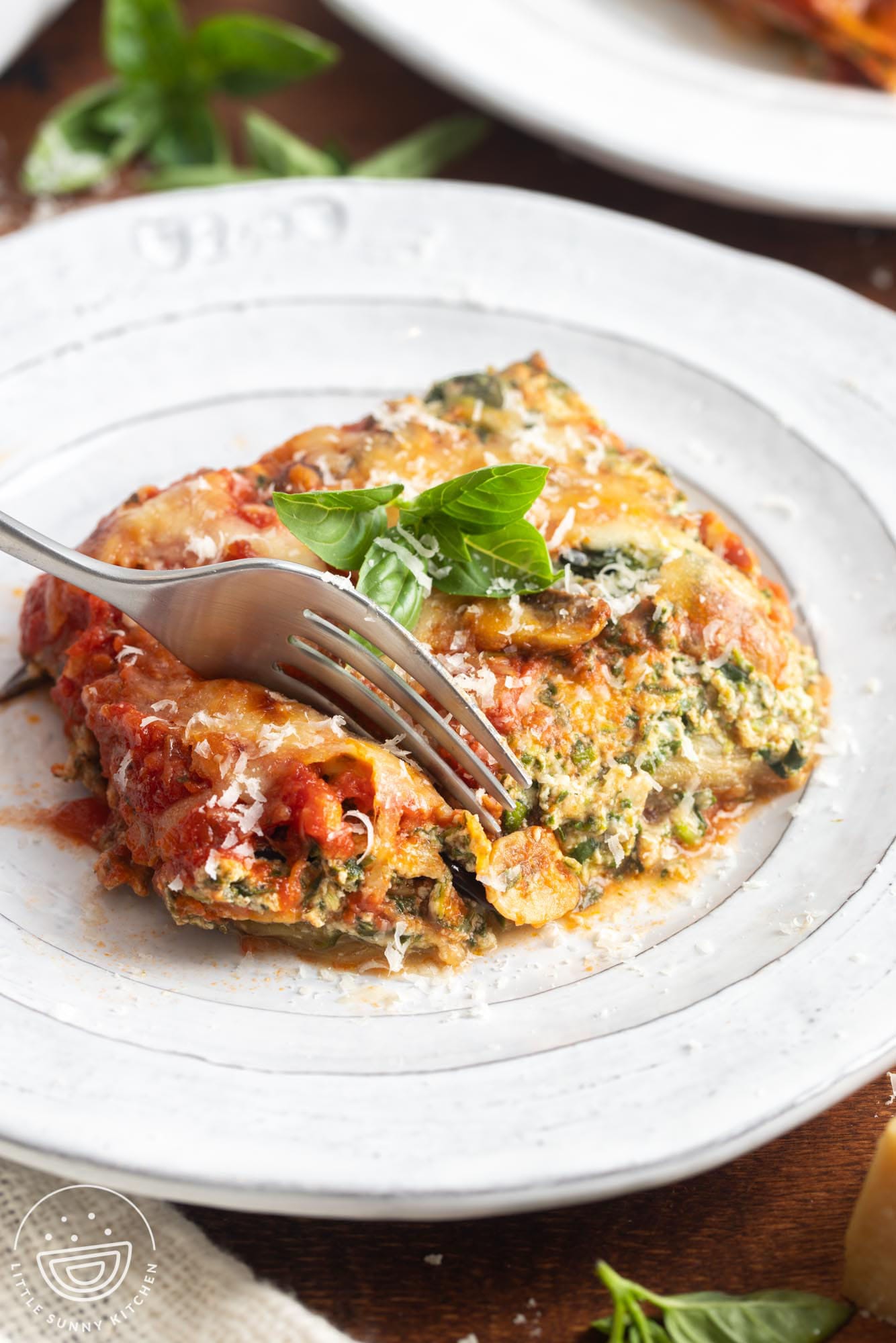 a square piece of eggplant lasagna made with cheese and tomato sauce on a plate. A fork is picking up a bite.