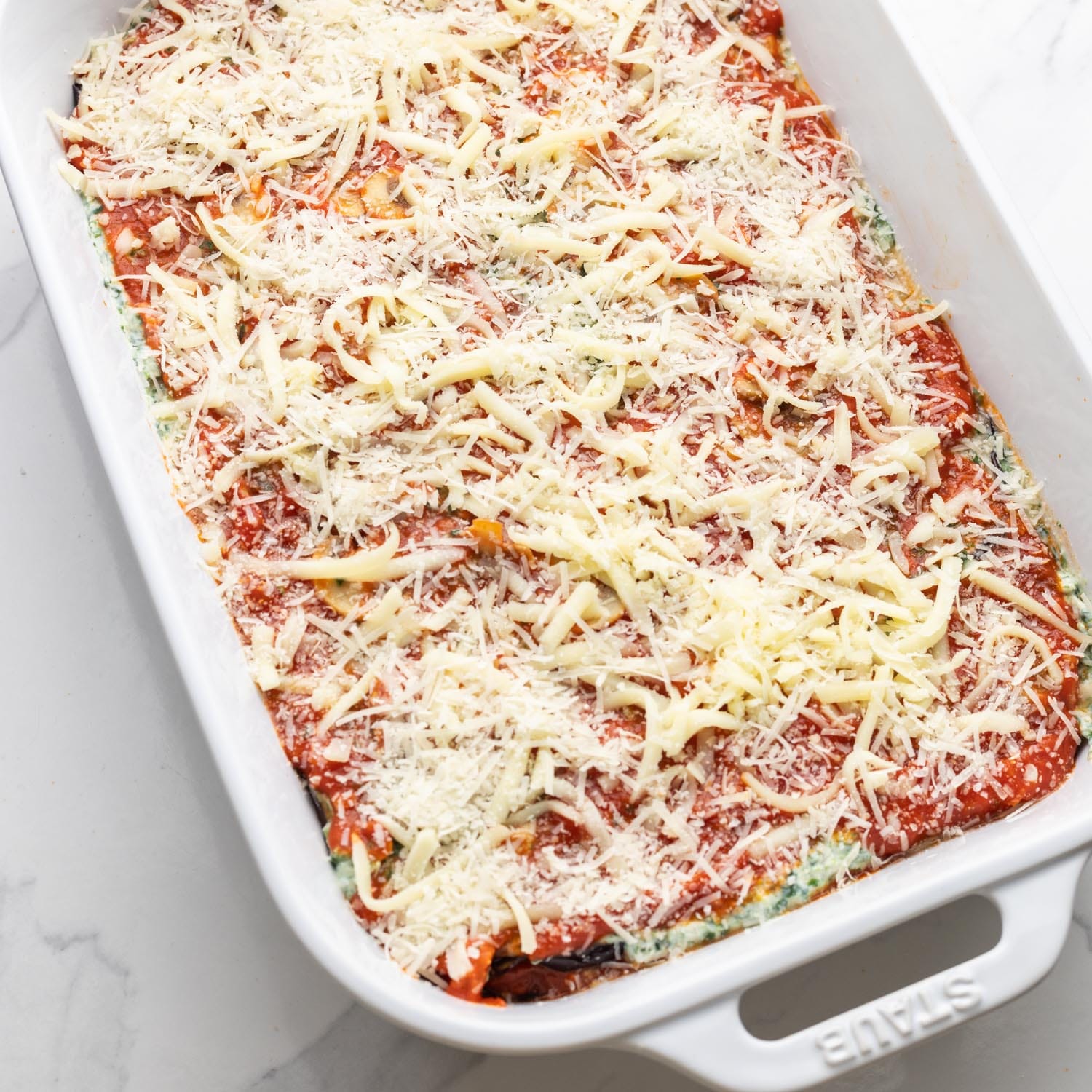 a white baking dish of eggplant lasagna topped with shredded cheese, not baked yet.