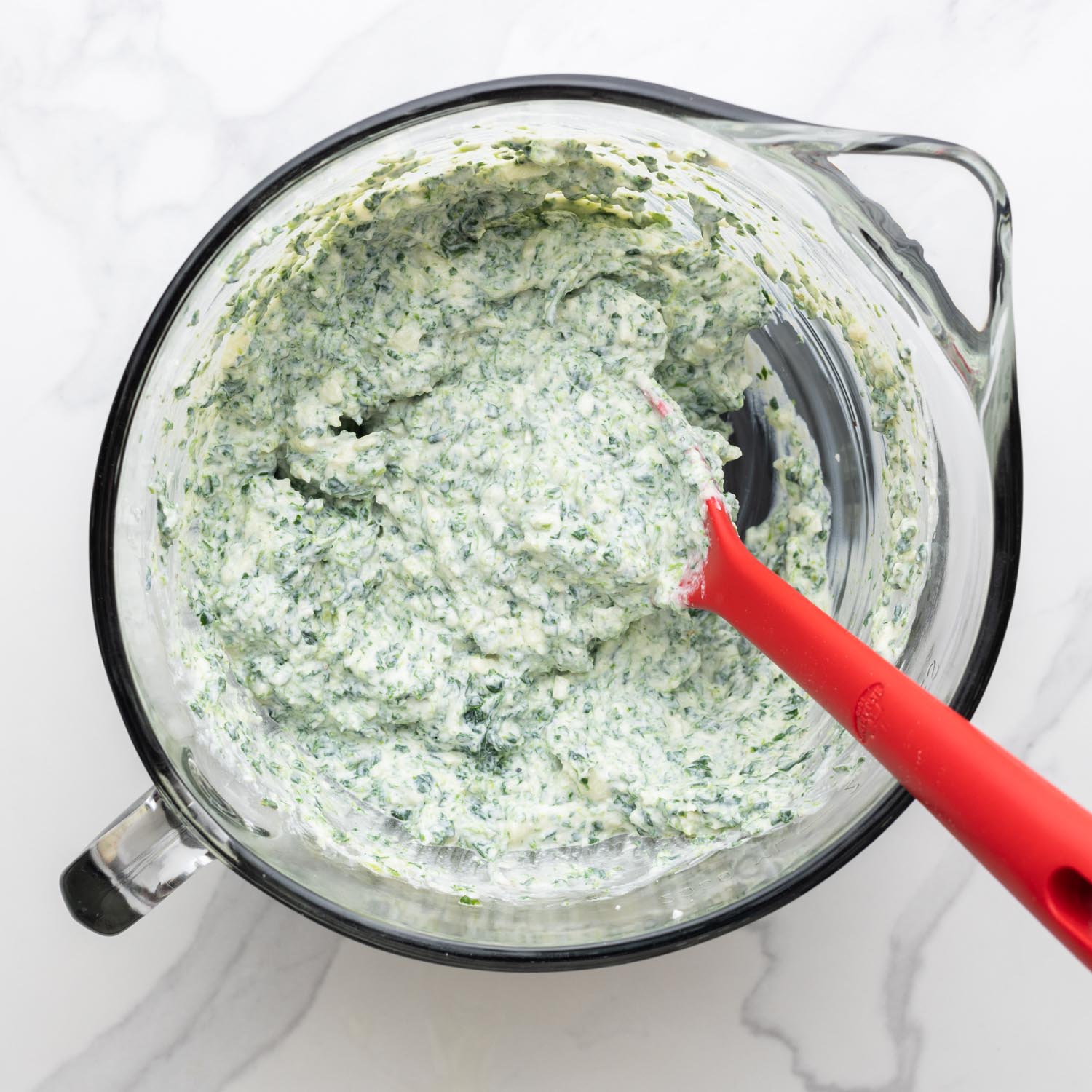 ricotta cheese mixed with herbs in a glass mixing bowl.