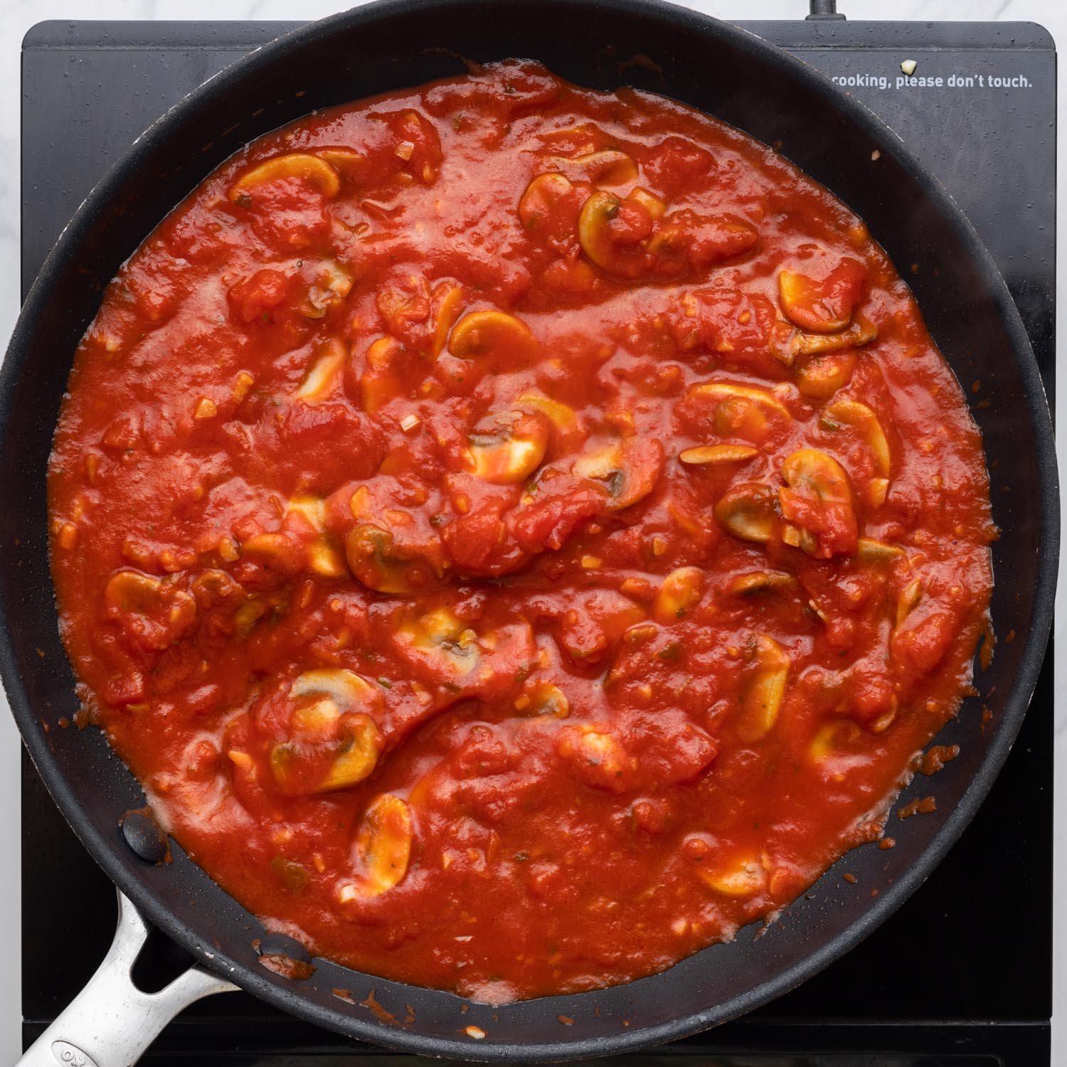 tomato sauce with sliced mushrooms cooking in a nonstick skillet.